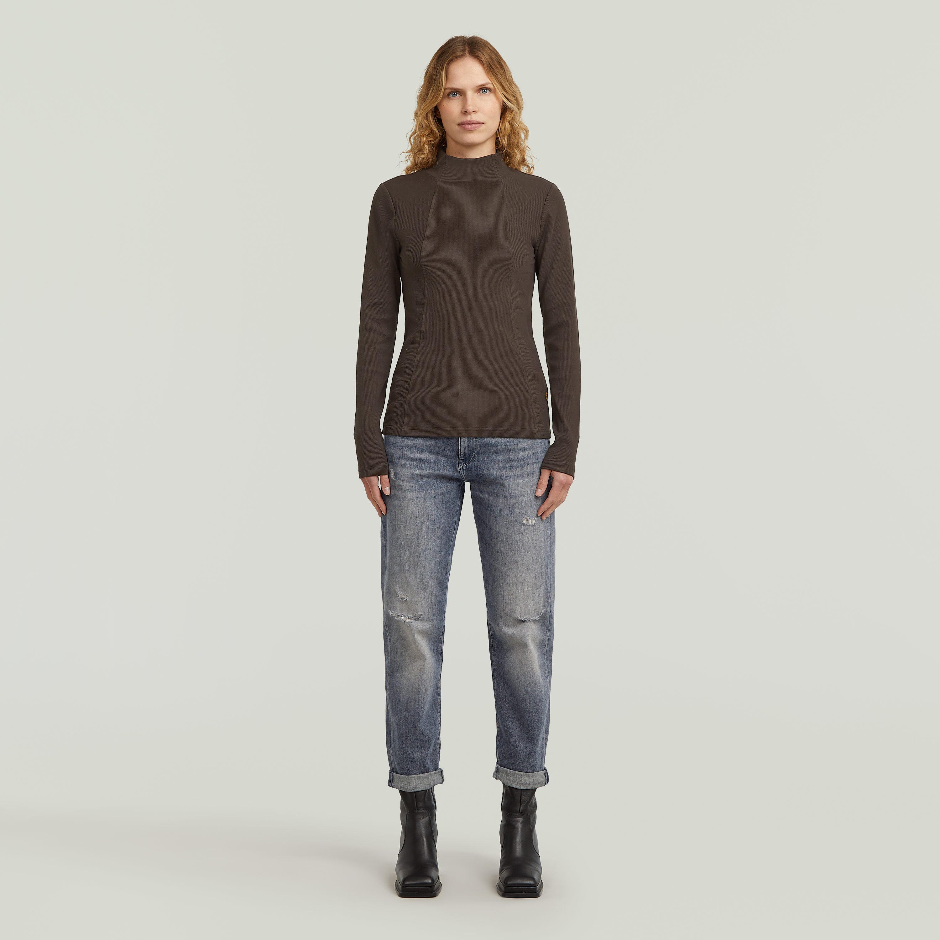 Model wearing low rise boyfriend jeans with dark shirt and boots, showcasing a casual look.