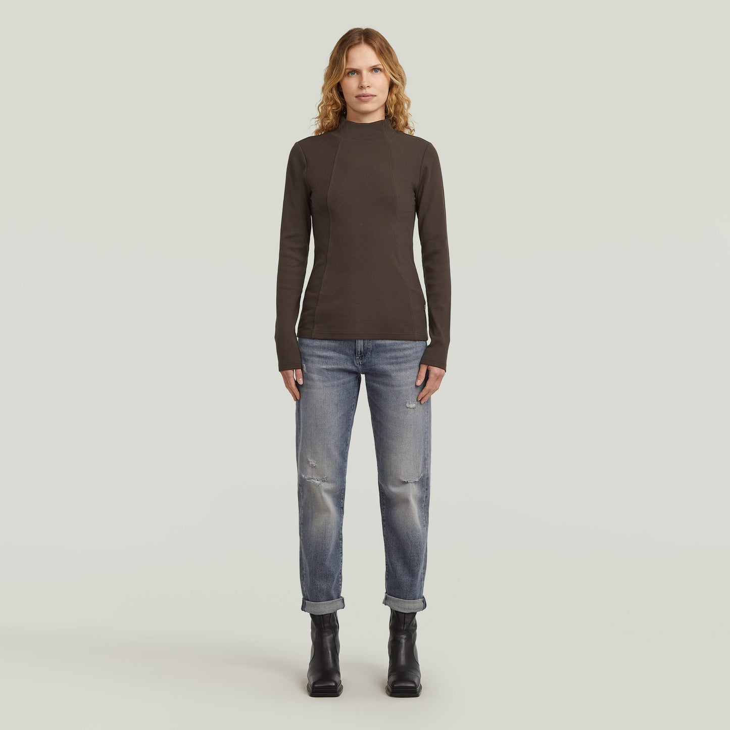 Model wearing low rise boyfriend jeans with dark shirt and boots, showcasing a casual look.