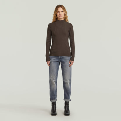 Model wearing low rise boyfriend jeans with dark shirt and boots, showcasing a casual look.