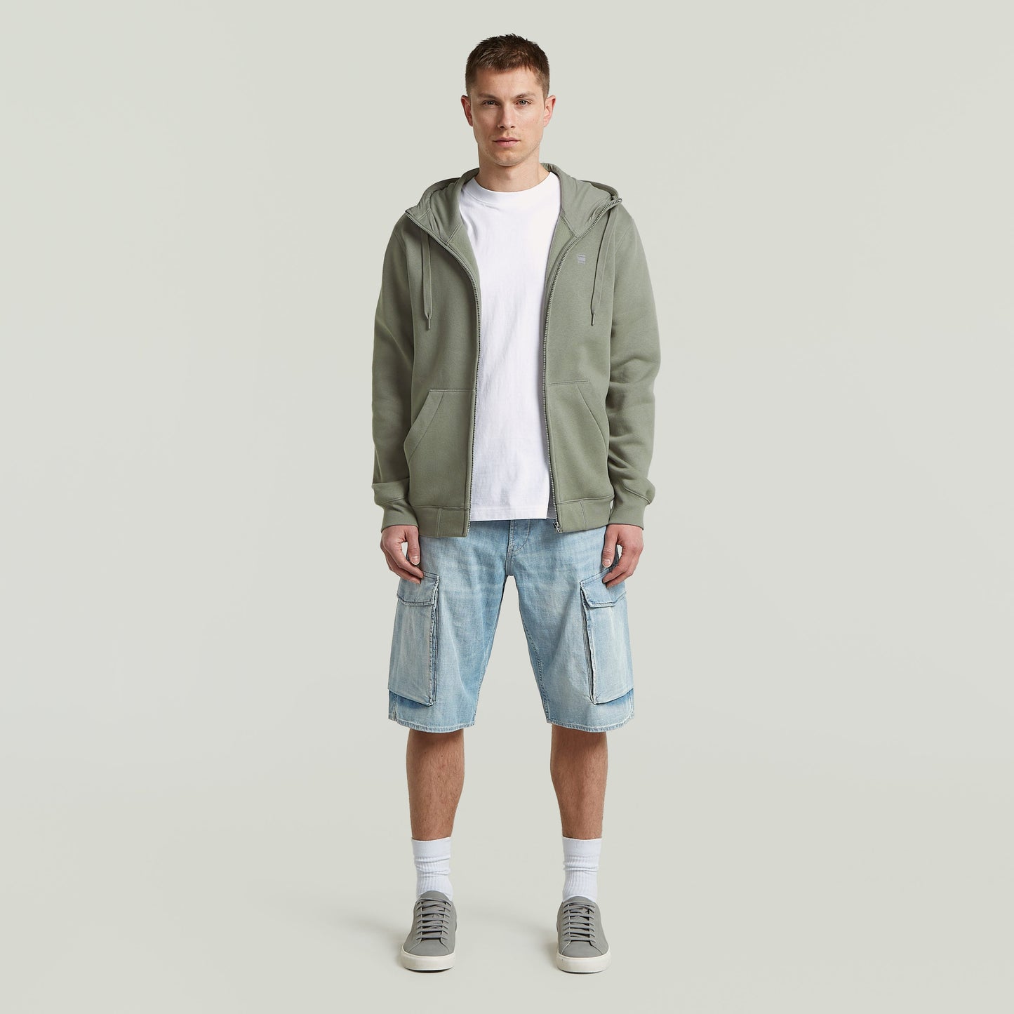 Modelo masculino usando sudadera premium hooded zip sweatshirt con pantalones cortos y zapatillas deportivas.