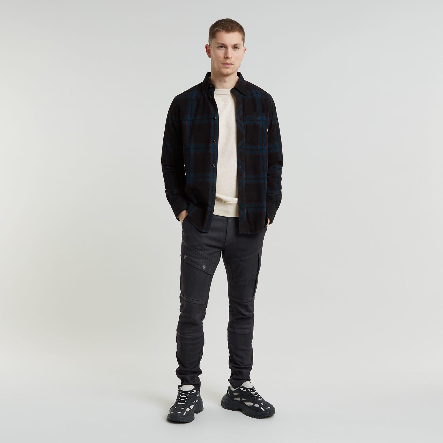 Hombre vistiendo jeans 3D skinny para mujer con chaqueta de cuadros y zapatillas deportivas.