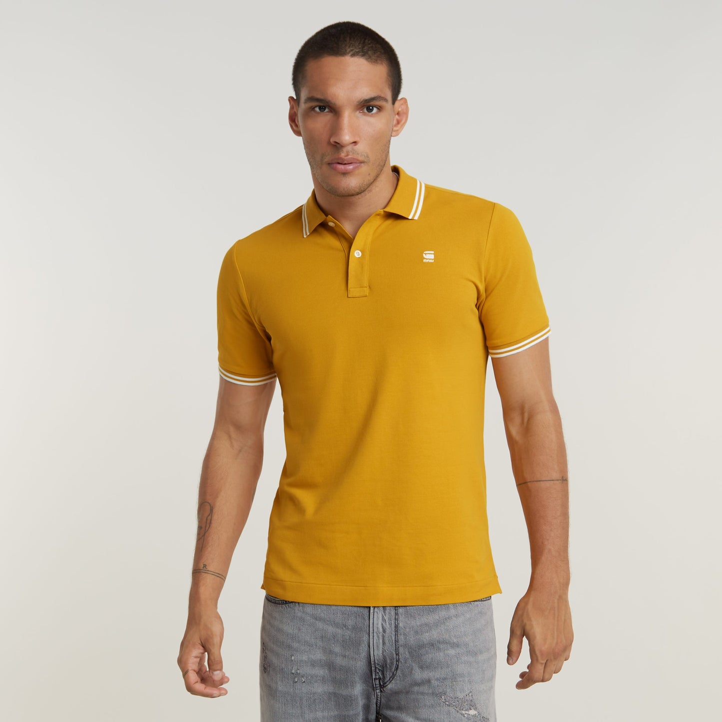 Modelo masculino usando un polo dunda slim stripe de color mostaza con cuello y puños acanalados.