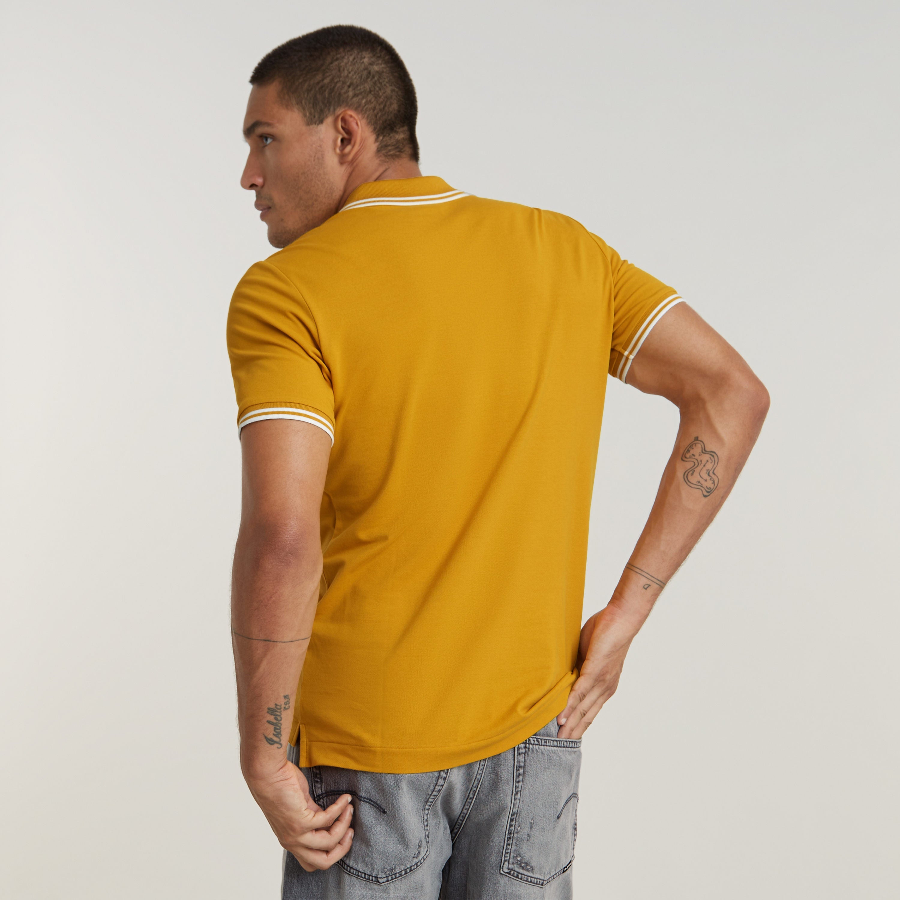 Hombre de espaldas vistiendo una camisa polo Dunda Slim Stripe color mostaza.