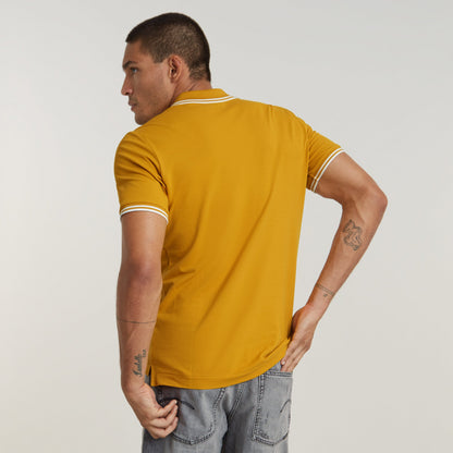 Hombre de espaldas vistiendo una camisa polo Dunda Slim Stripe color mostaza.