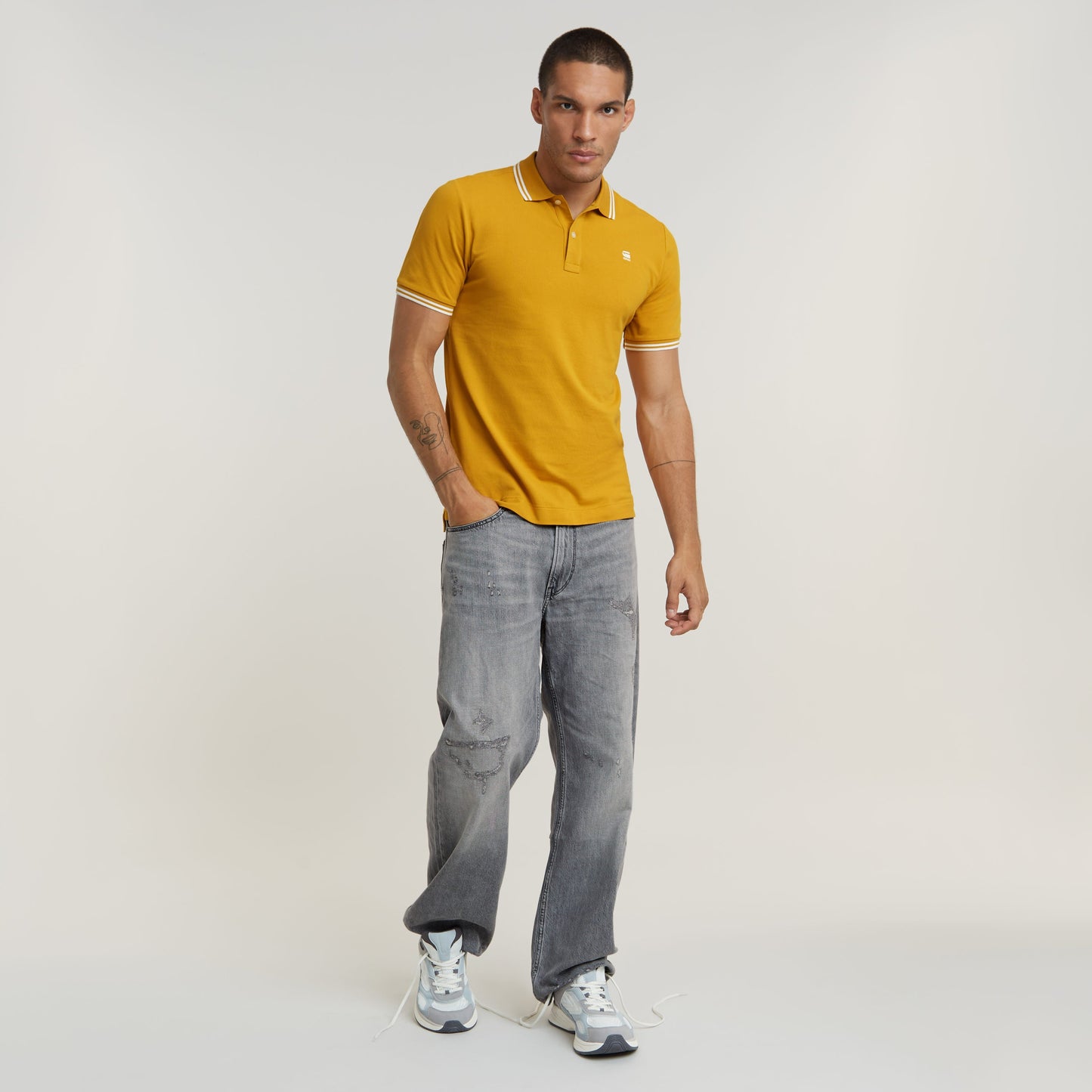 Hombre usando una camiseta polo Dunda Slim Stripe amarilla con detalles de rayas, combinada con jeans y zapatillas.