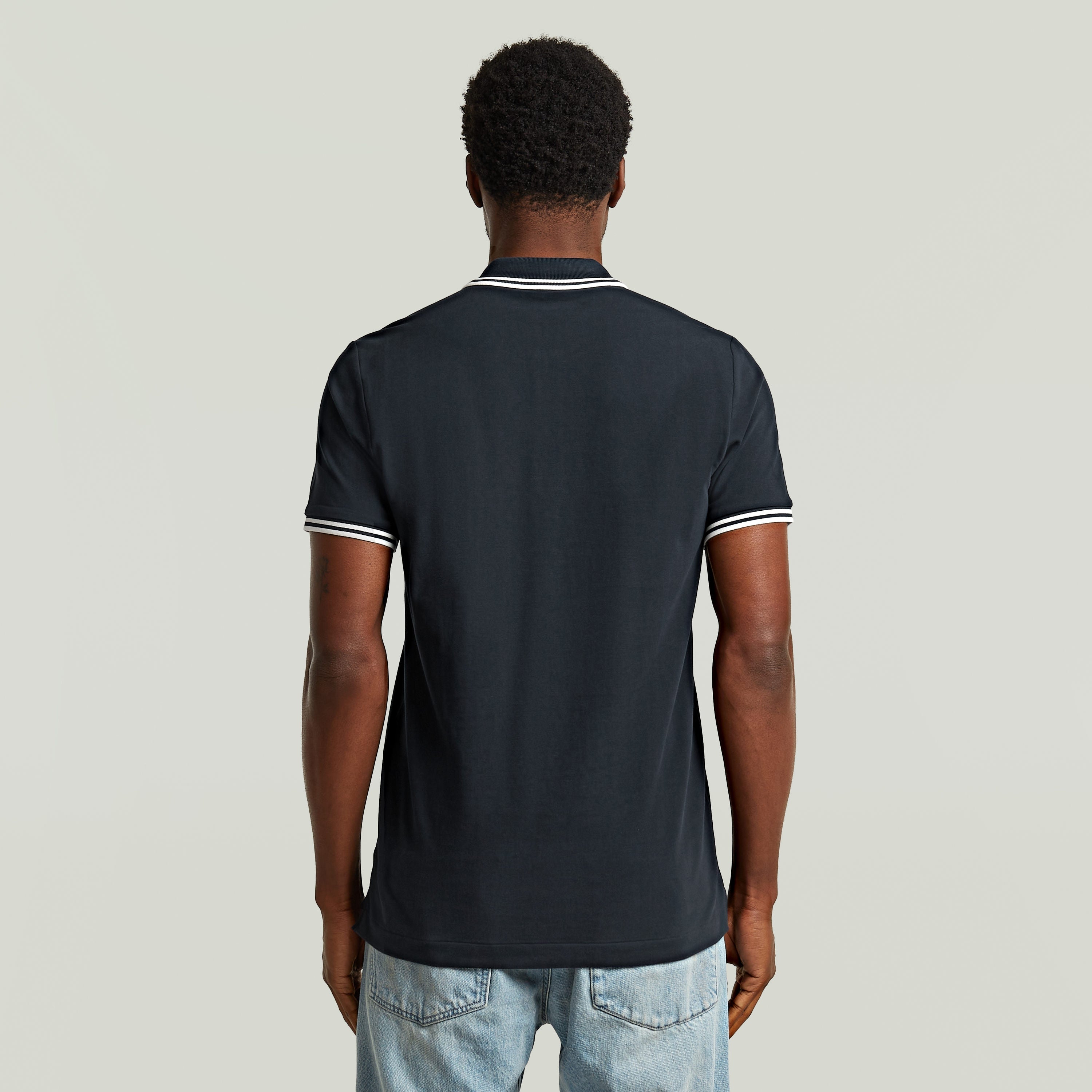 Back view of the Polo Dunda Slim Stripe, a slim stripe polo shirt in dark blue with stylish details.