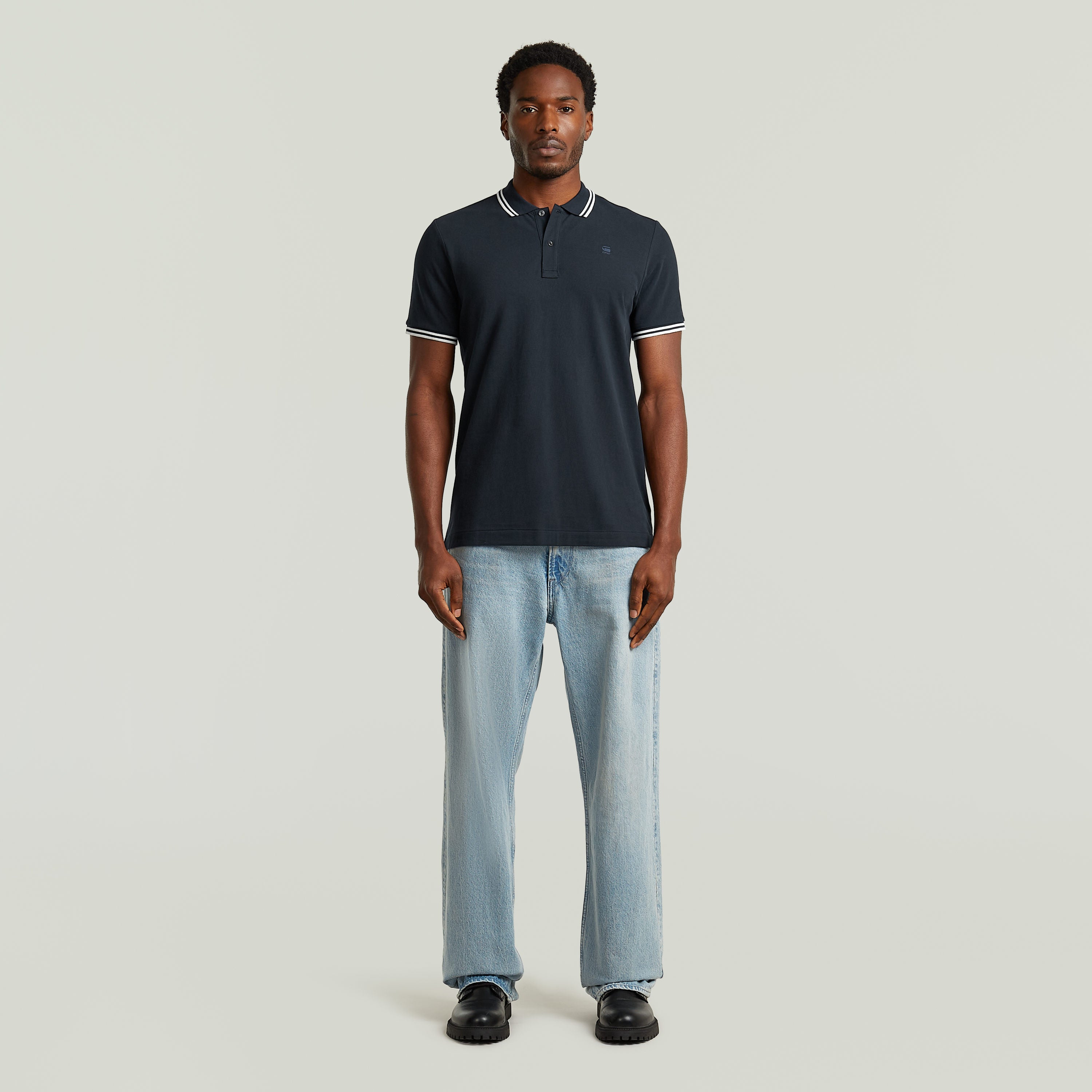 Hombre usando un slim stripe polo shirt azul oscuro con detalles en el cuello y pantalones claros.