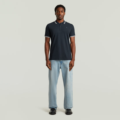 Hombre usando un slim stripe polo shirt azul oscuro con detalles en el cuello y pantalones claros.