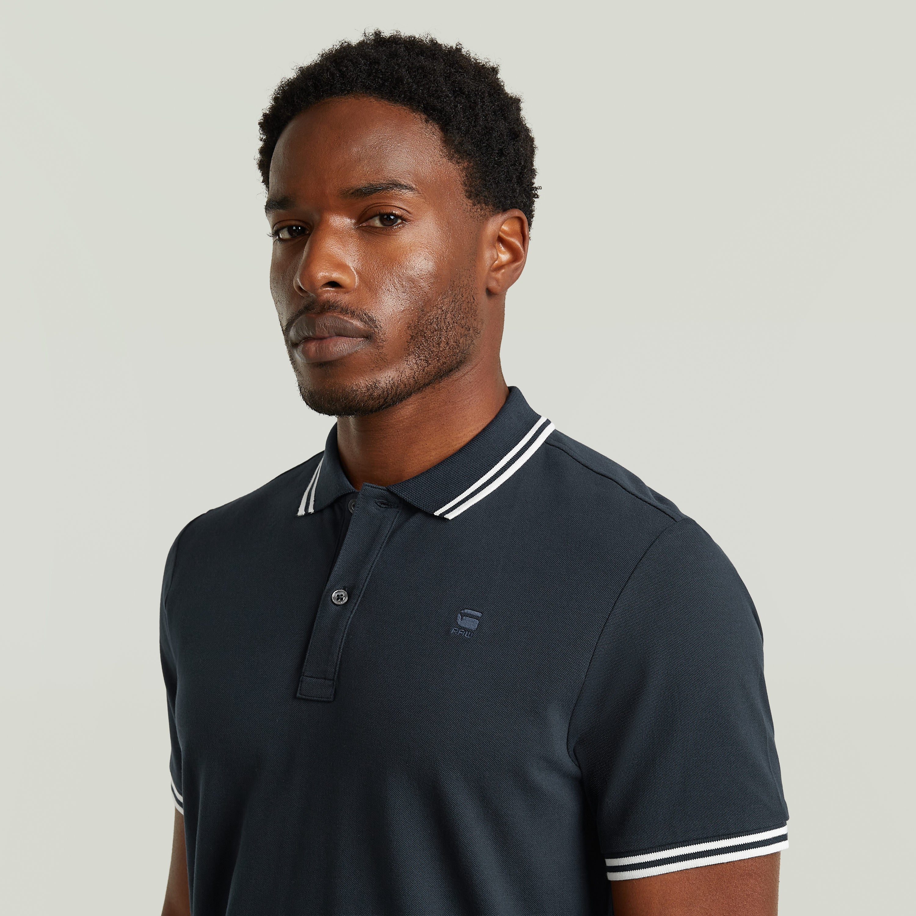 Modelo usando un polo Dunda Slim Stripe, camiseta slim stripe polo shirt, color azul oscuro con detalles en el cuello.