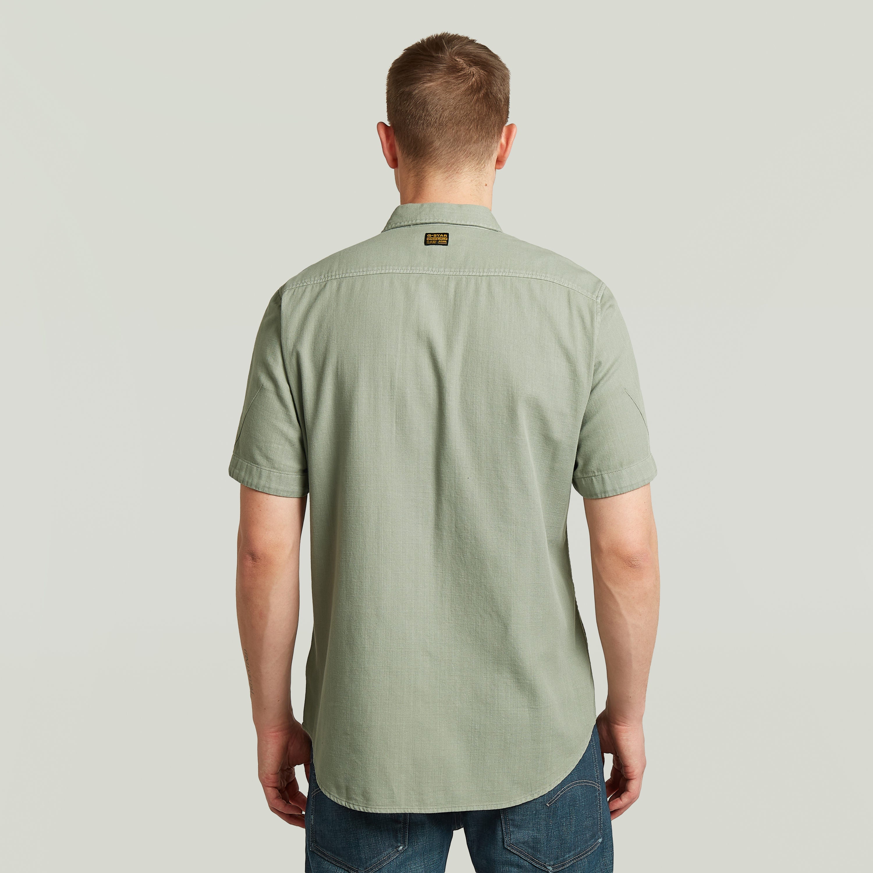 Hombre de espaldas con la camisa Marine Slim fit, color verde, corte ajustado y con bajo redondeado.