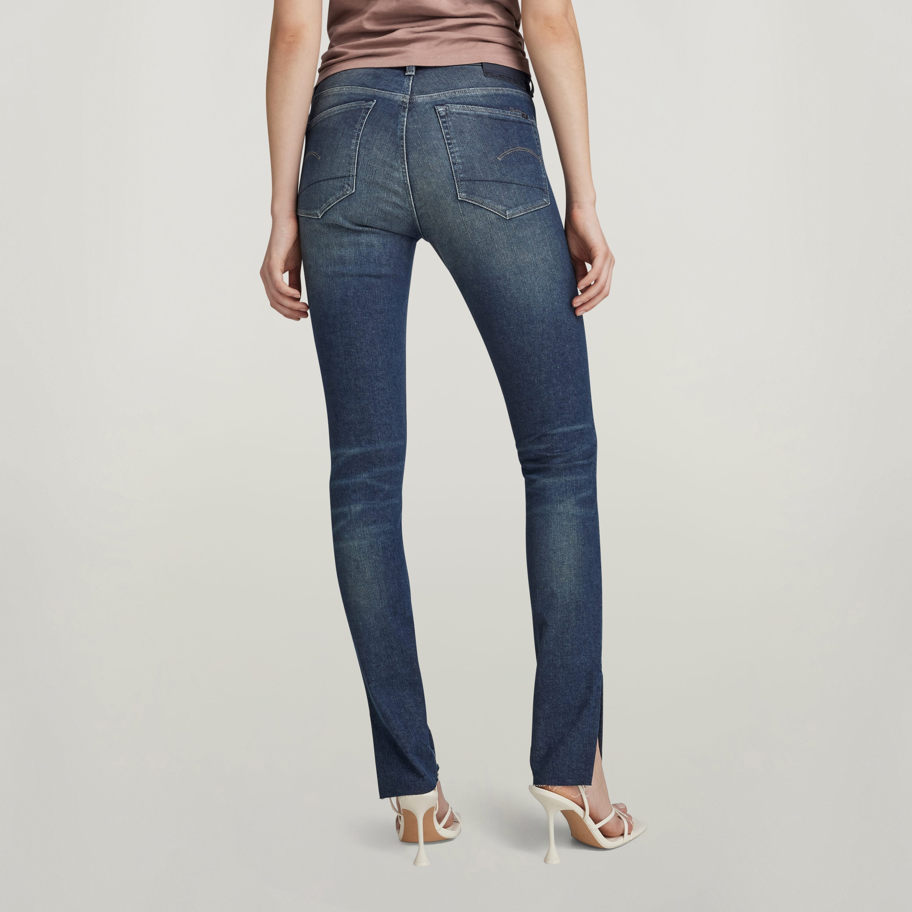 Mujer usando jeans 3301 skinny slit desde atrás, mostrando la abertura corta en la pierna y el diseño ajustado.