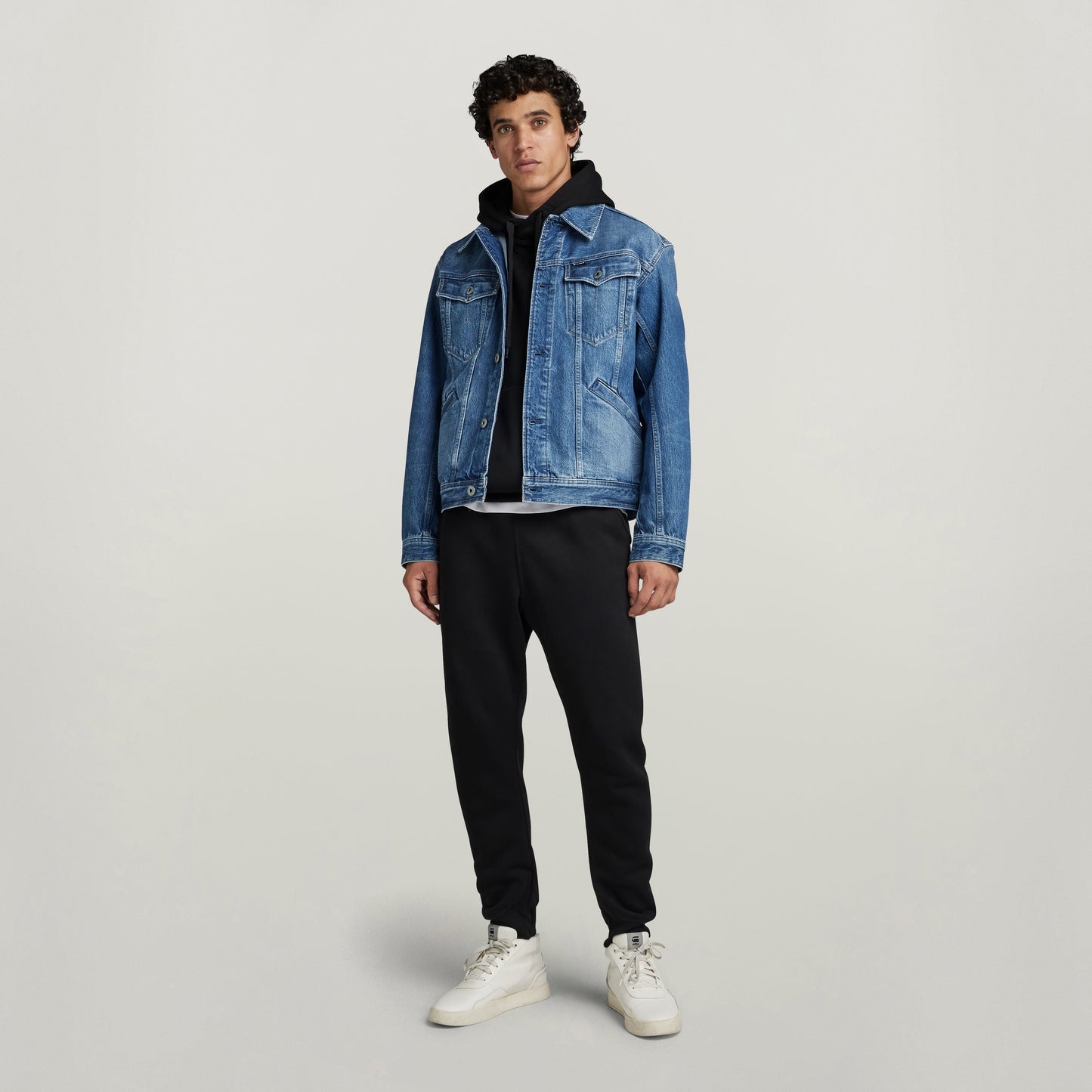 Modelo usando chaqueta unisex Flight Combat denim azul con pantalones negros y zapatillas blancas.
