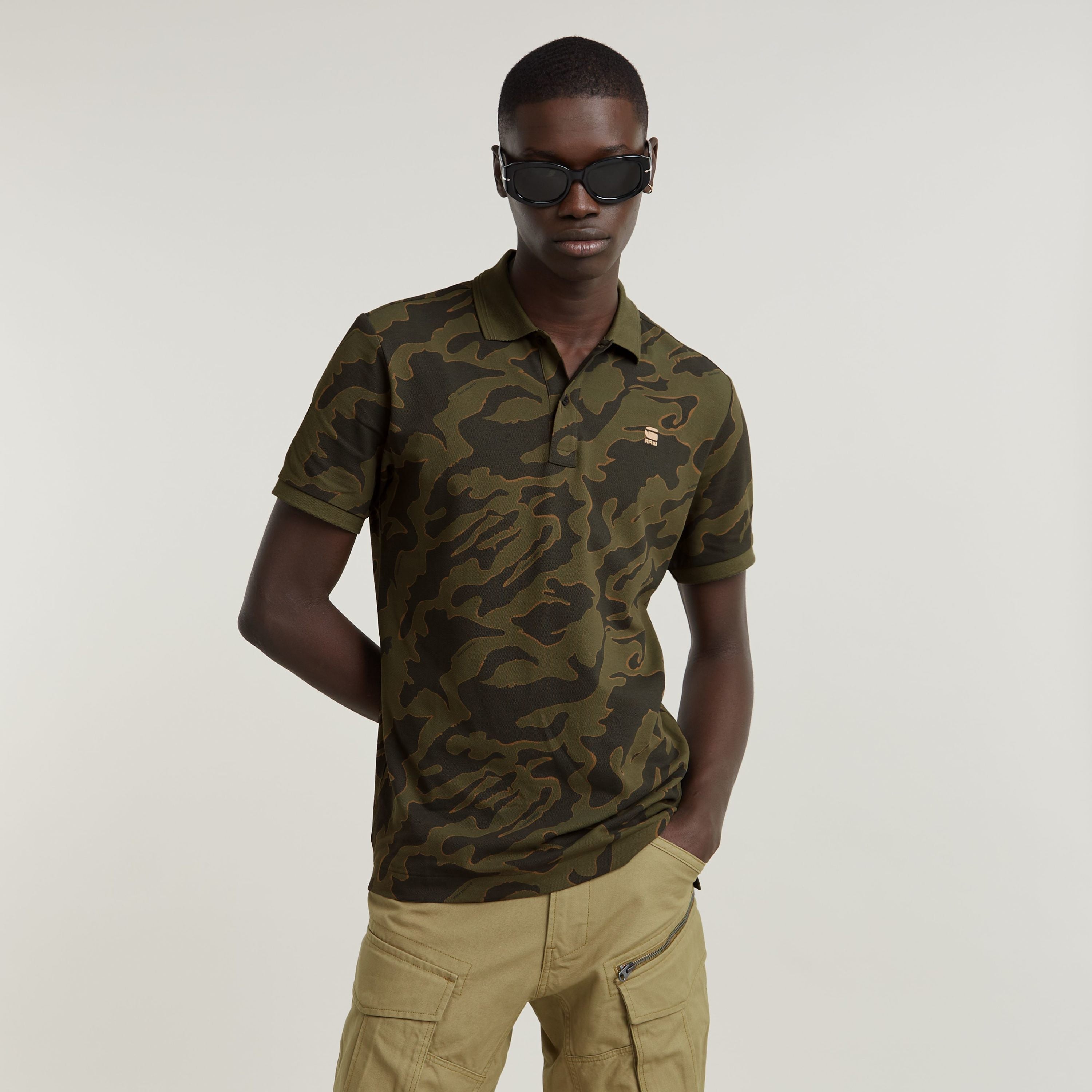 Model wearing a slim stripe polo shirt with camouflage print and sunglasses, showcasing modern style.