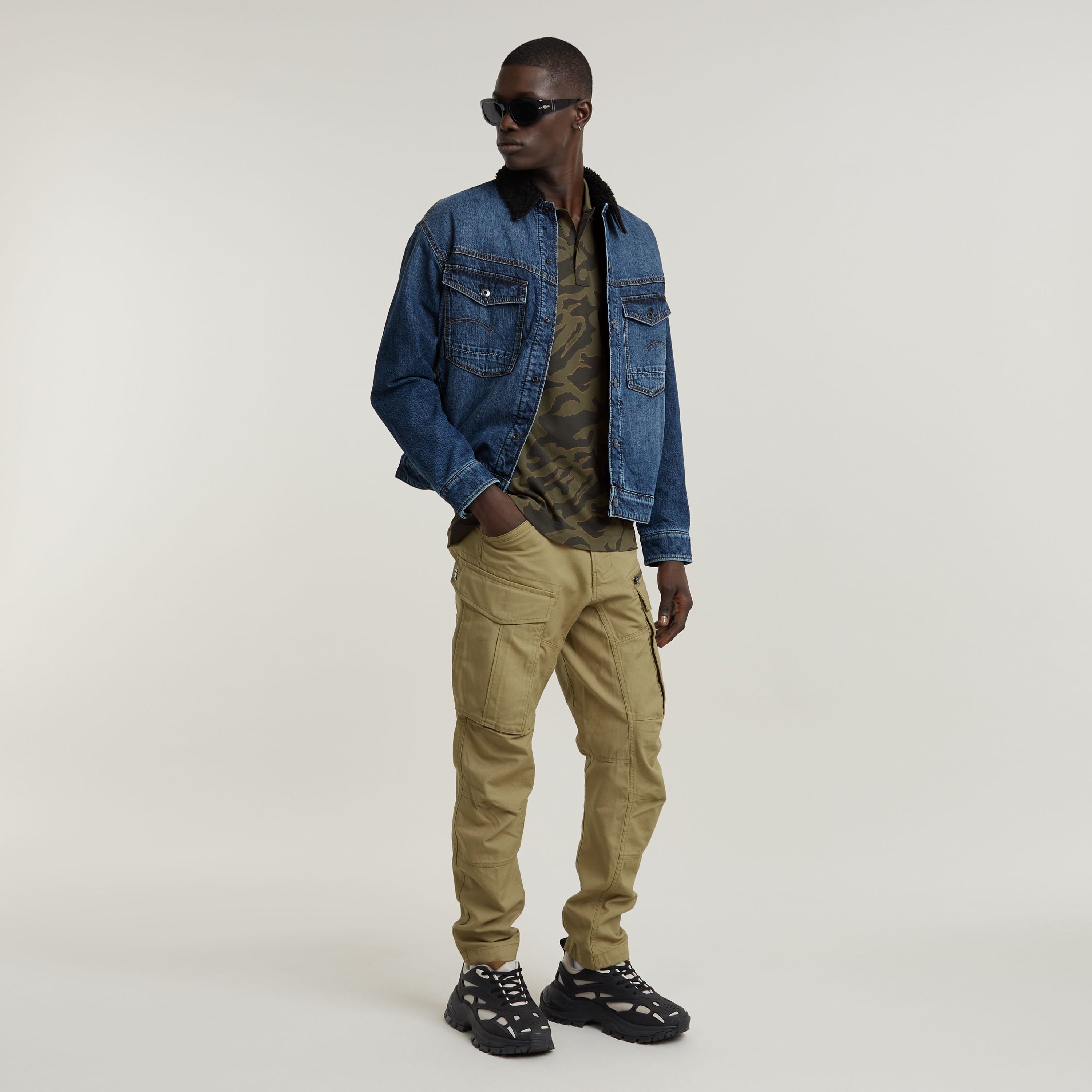 modelo con gafas de sol usando una camisa polo slim stripe, chaqueta de mezclilla y pantalones cargo.