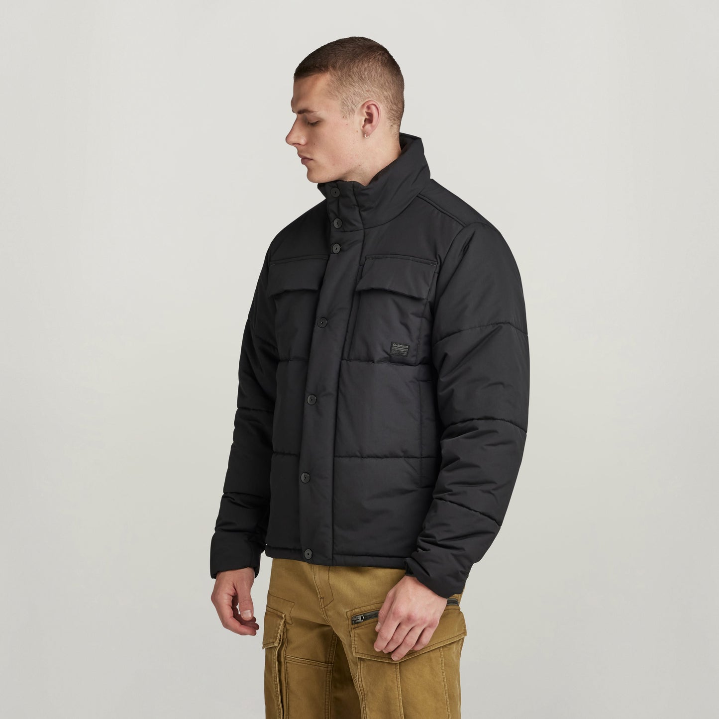 Hombre usando chaqueta acolchada impermeable Foundation negra, con cuello alzado y ajuste en el bajo.