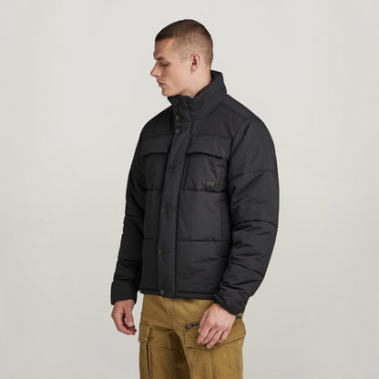 Hombre usando chaqueta acolchada impermeable Foundation negra, con cuello alzado y ajuste en el bajo.