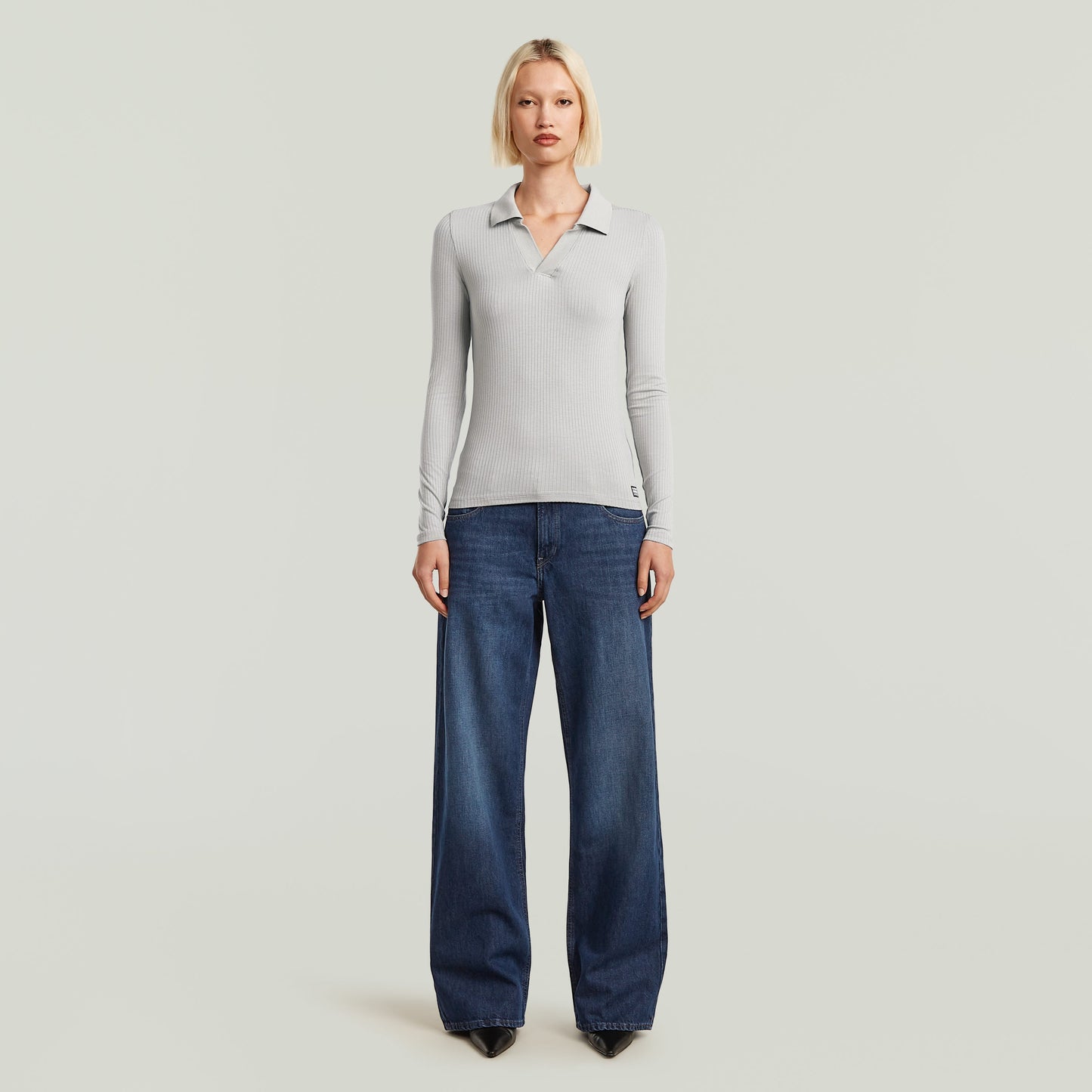 Model wearing low waist loose jeans with a fitted long-sleeve polo shirt, showcasing a stylish casual look.
