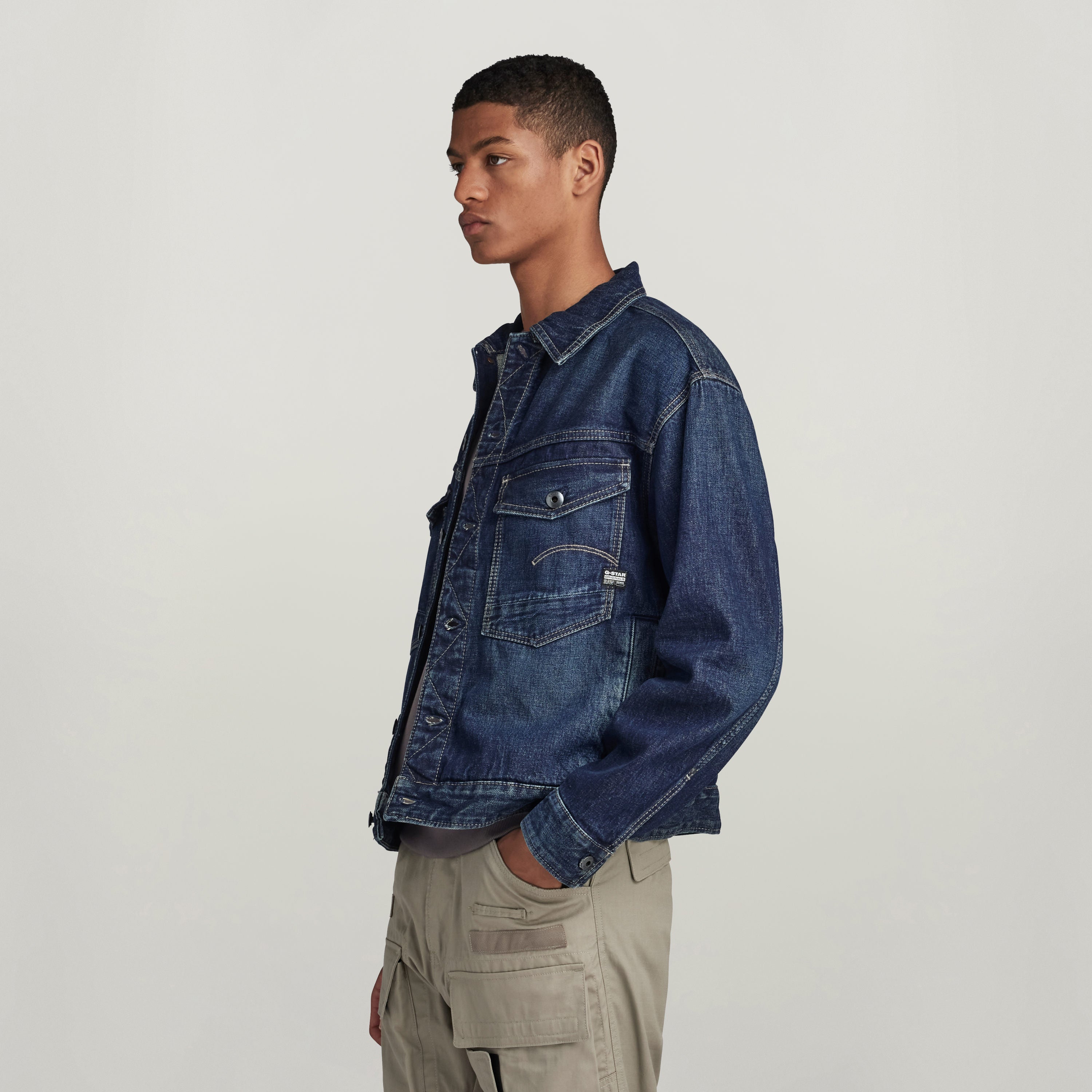 Hombre usando chaqueta denim Dakota de corte recto con bolsillos y cierre de botón en fondo neutral.