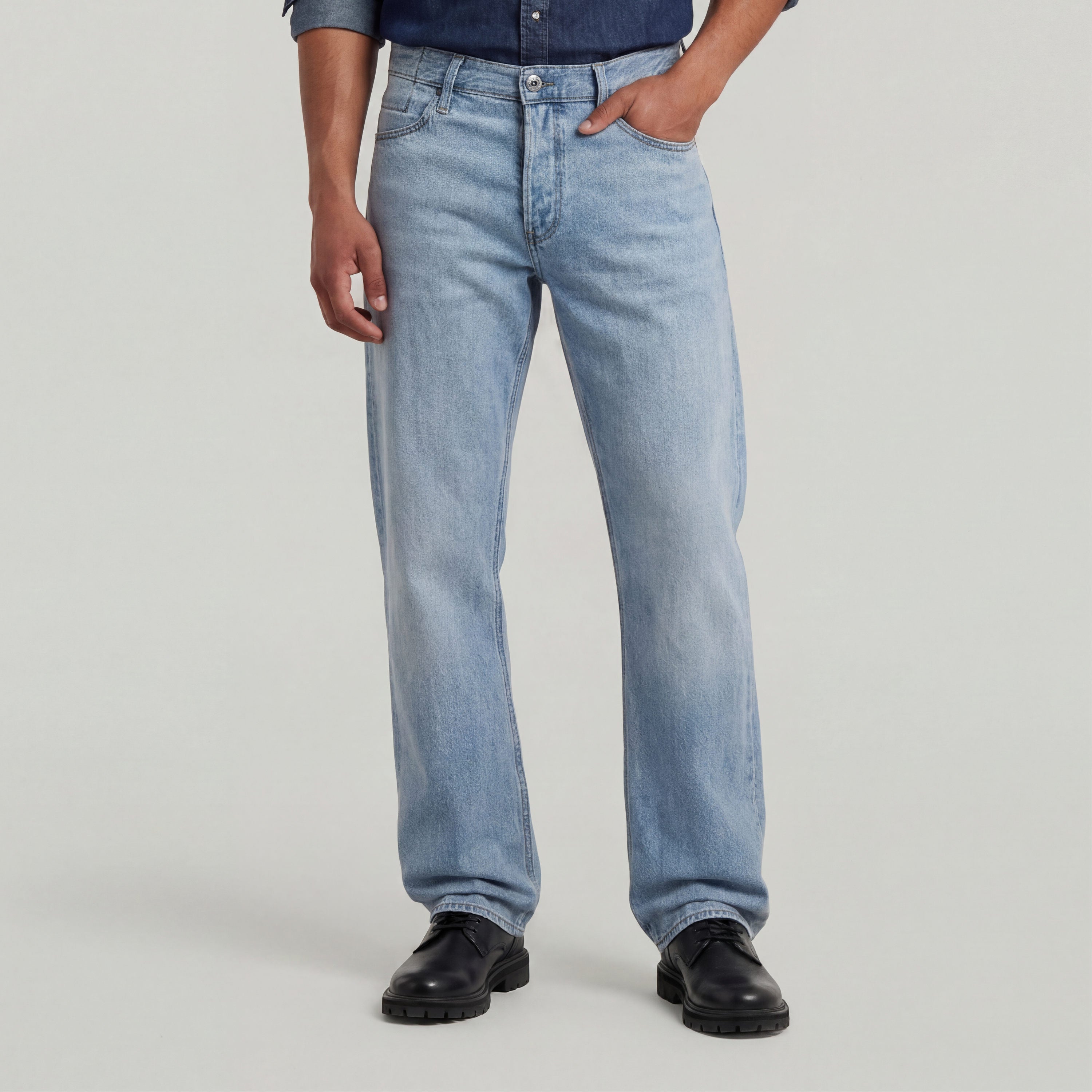 Modelo usando jeans Dakota regular straight en un tono claro, combinados con una camisa oscura y zapatos negros.
