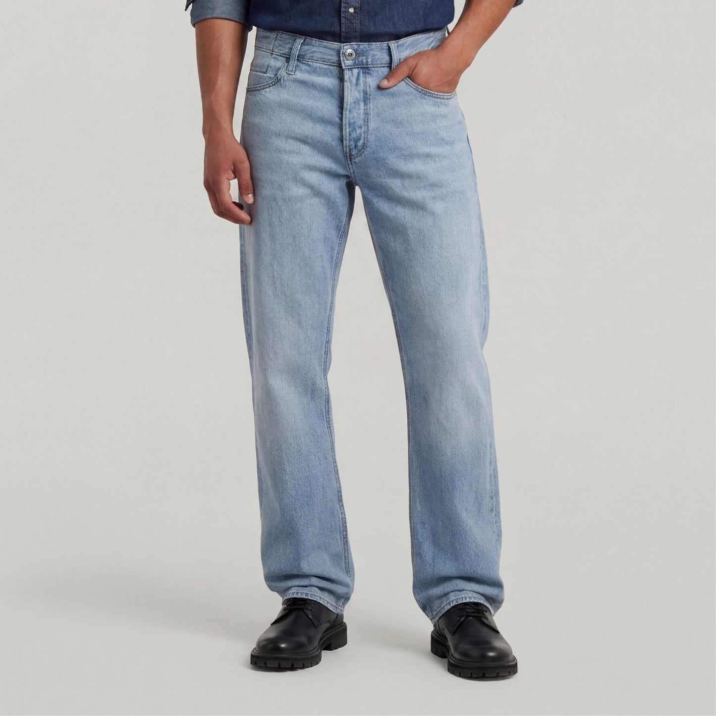Modelo usando jeans Dakota regular straight en un tono claro, combinados con una camisa oscura y zapatos negros.