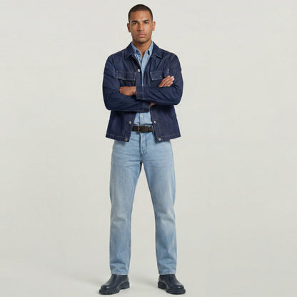 Hombre luciendo jeans Dakota regular straight, con chaqueta de mezclilla y camiseta, de pie frente a fondo neutro.