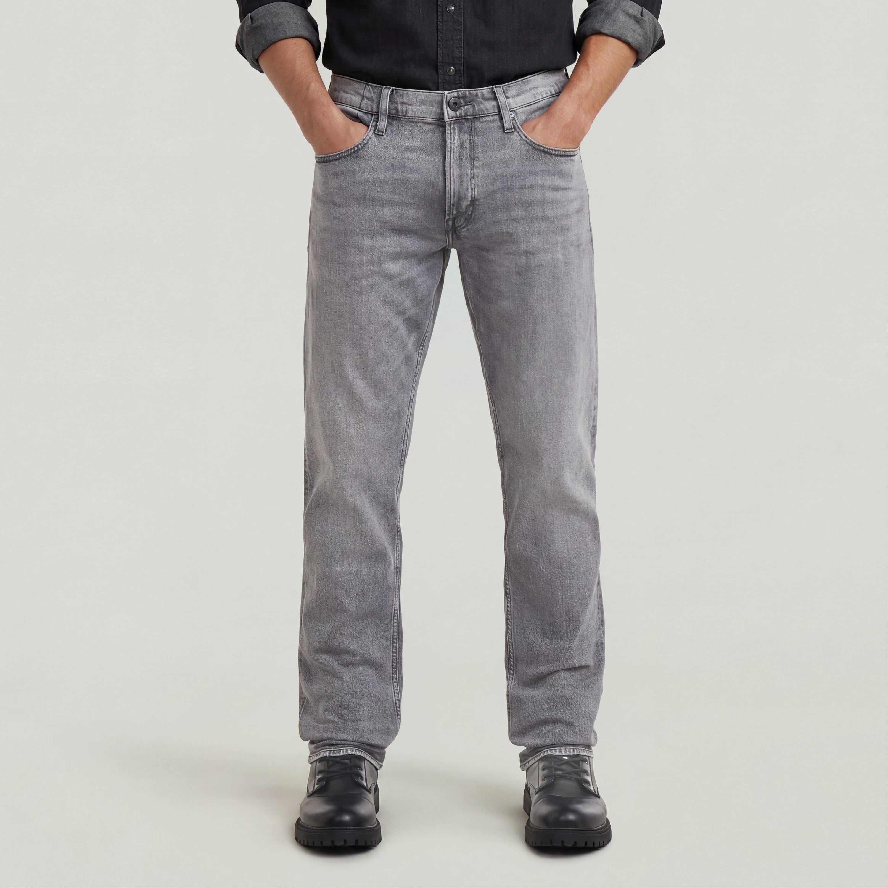 Hombre usando Jeans Mosa Straight en color gris con camisa negra y botas, mostrando un estilo casual y moderno.