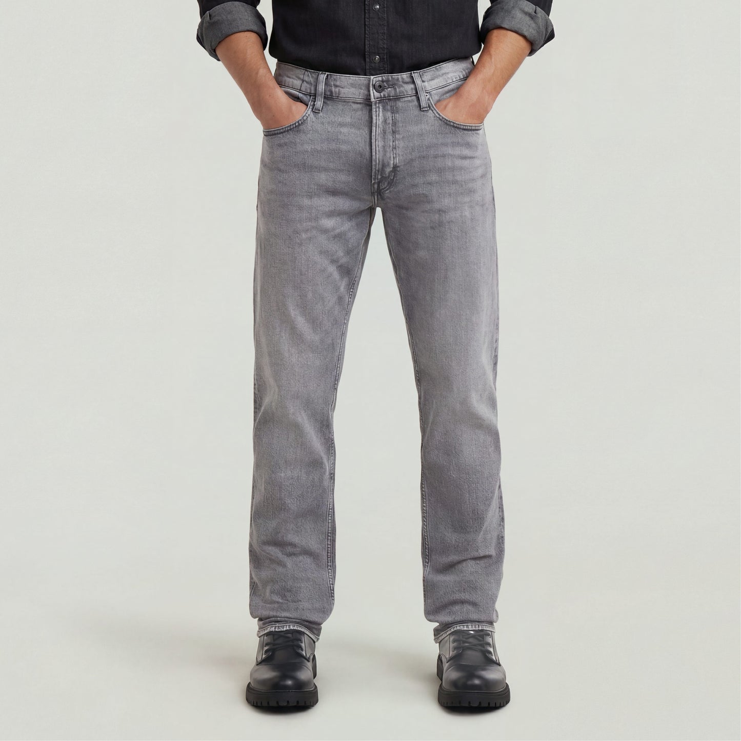 Hombre usando Jeans Mosa Straight en color gris con camisa negra y botas, mostrando un estilo casual y moderno.