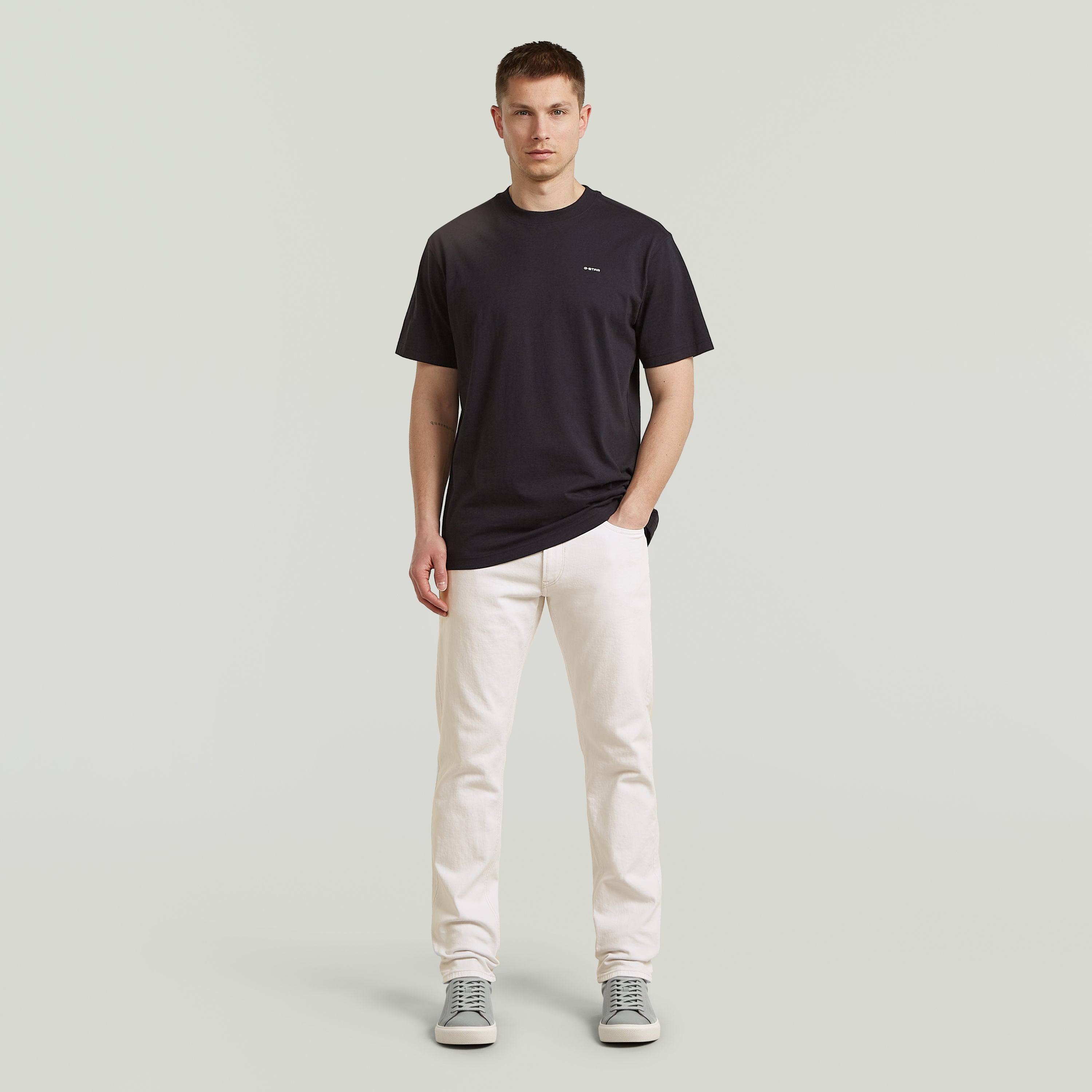 Modelo masculino vistiendo Mosa straight jeans en color blanco con camiseta negra y zapatillas grises.