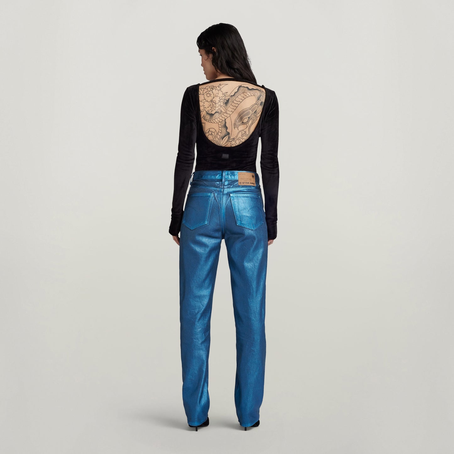 Mujer con jeans de talle alto, perneras rectas, de color azul brillante, vista posterior con diseño en la espalda.