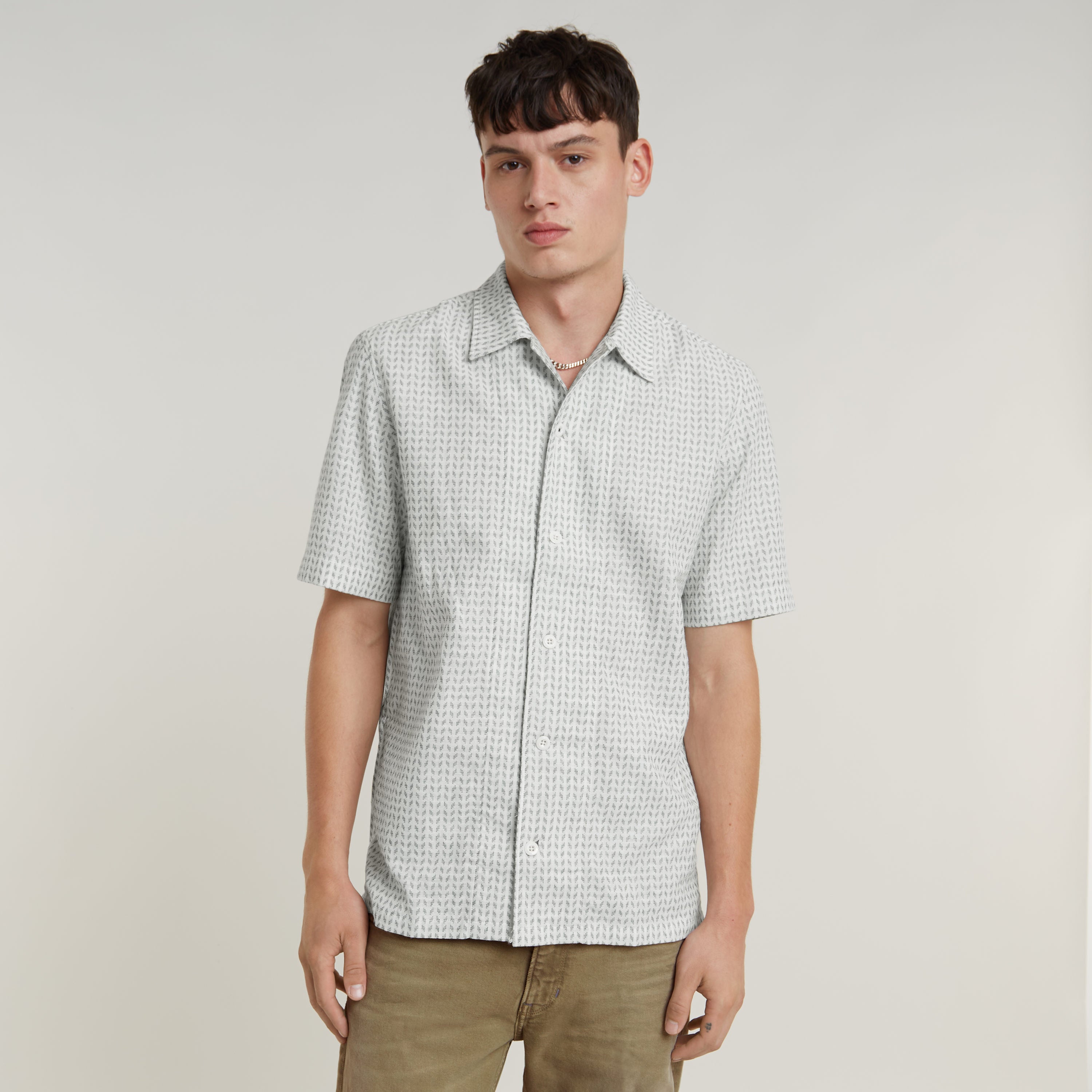 Modelo lleva camisa resort de corte recto con diseño de cuello plano y botones, en fondo claro con detalles sutiles.