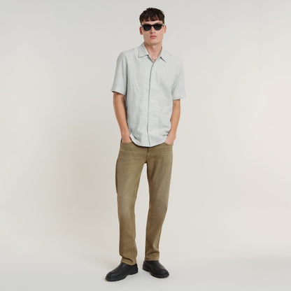 Camisa Resort de corte recto de diseño fresco con pantalones en tono tierra y gafas de sol en un fondo claro.