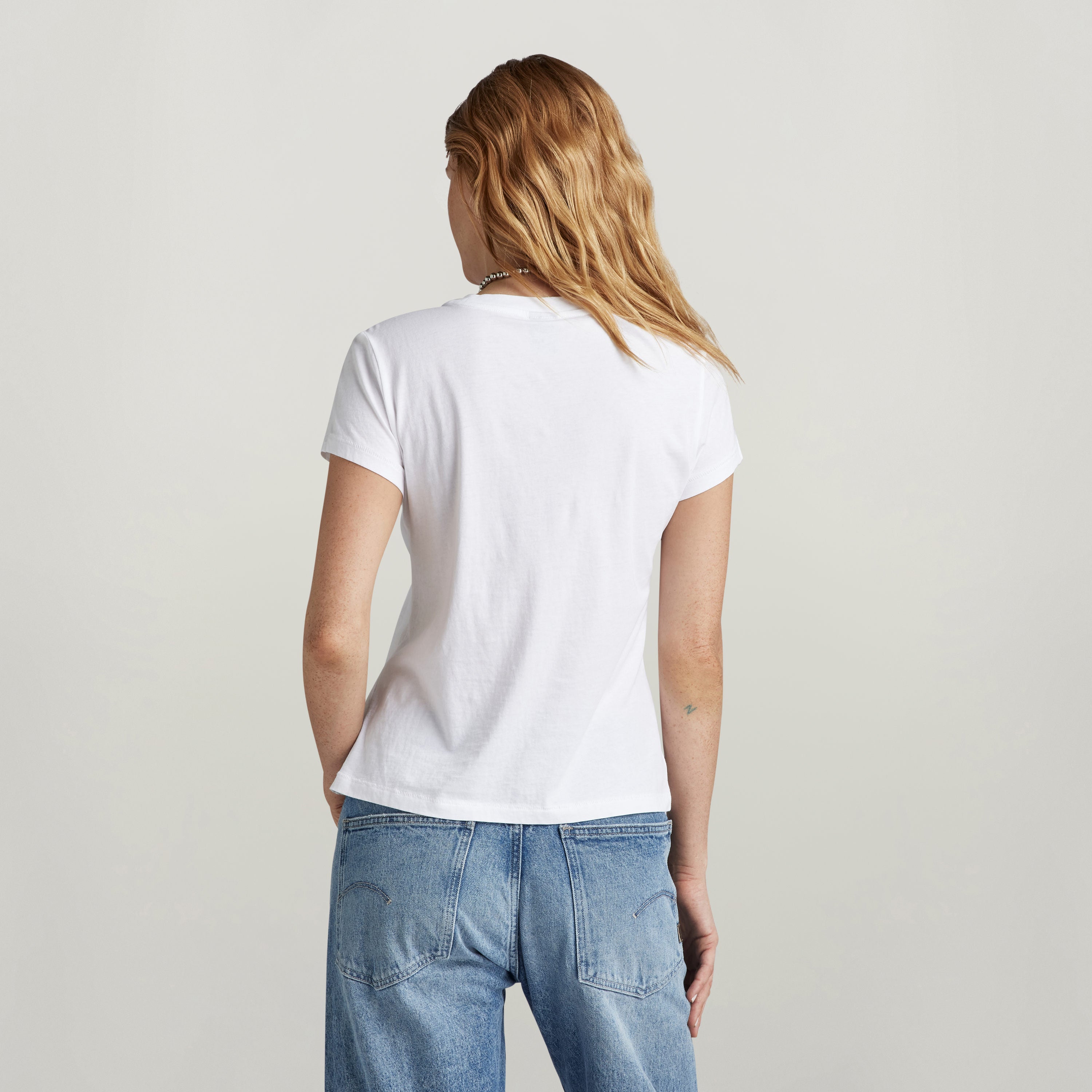 Back view of a woman wearing a top front seam shirt with embroidery in white.