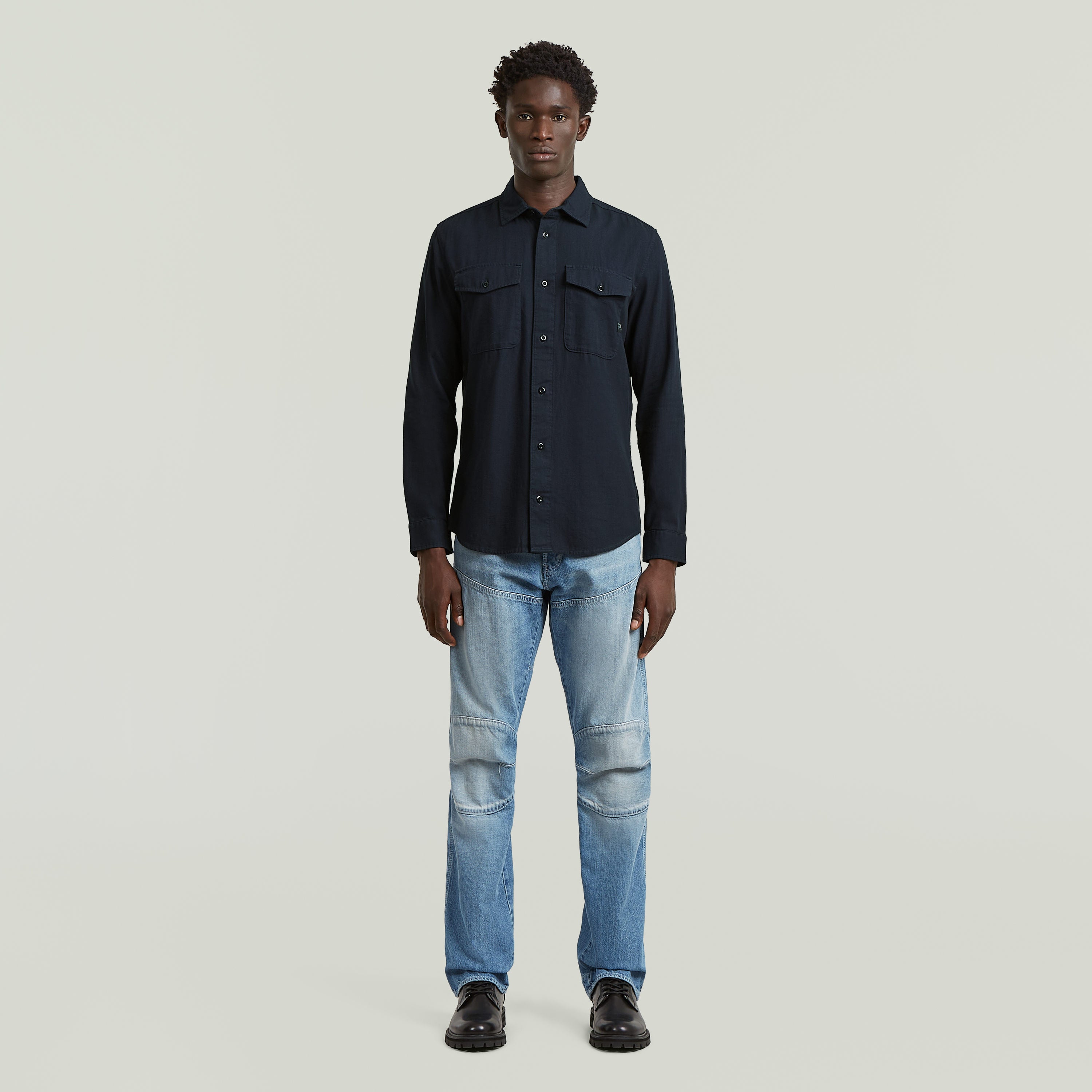 Hombre luciendo camisa marine slim azul, corte ajustado y bajo redondeado, en fondo claro.