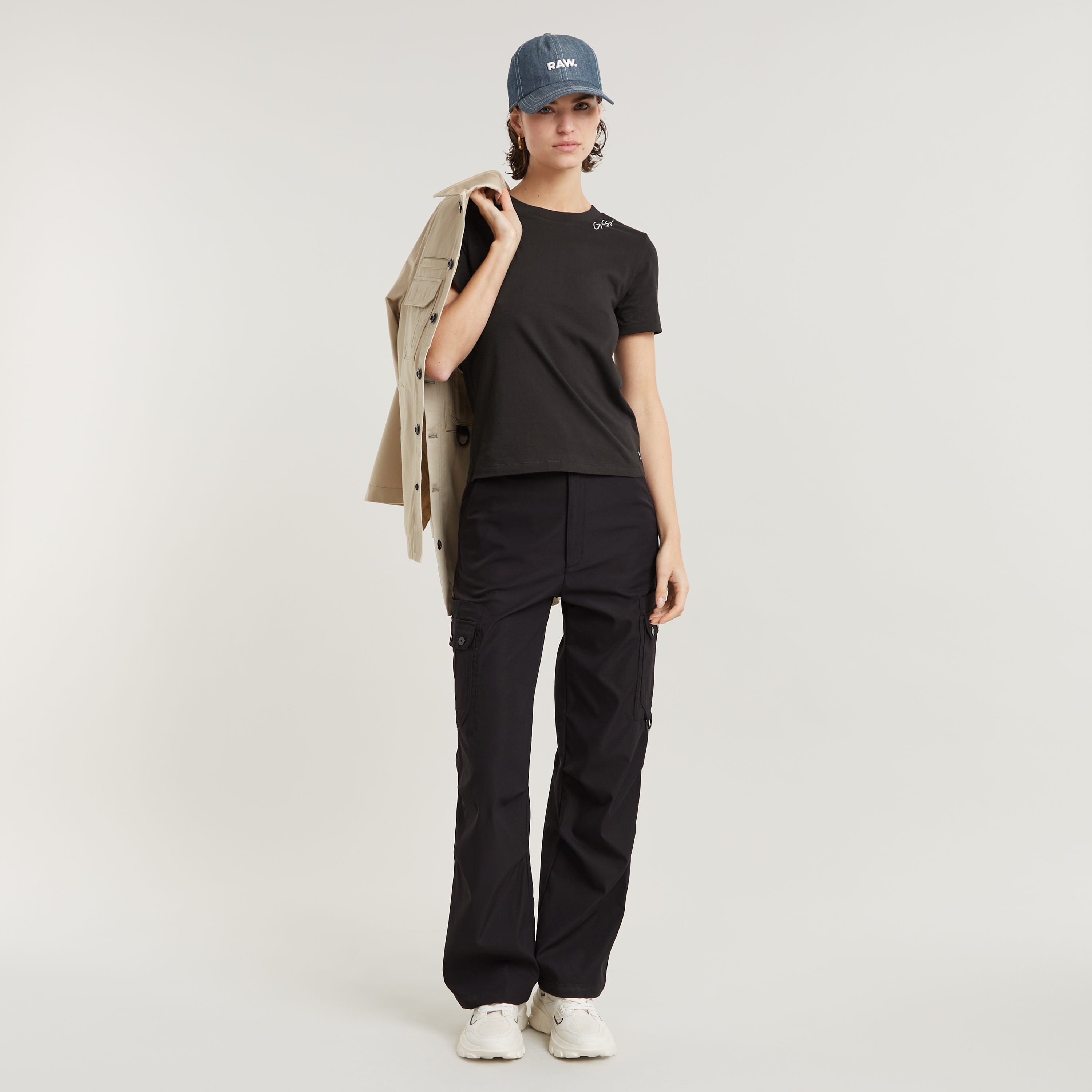 Modelo luciendo el top faux embroidered logo en negro, con pantalones cargo y gorra, en un fondo neutral.
