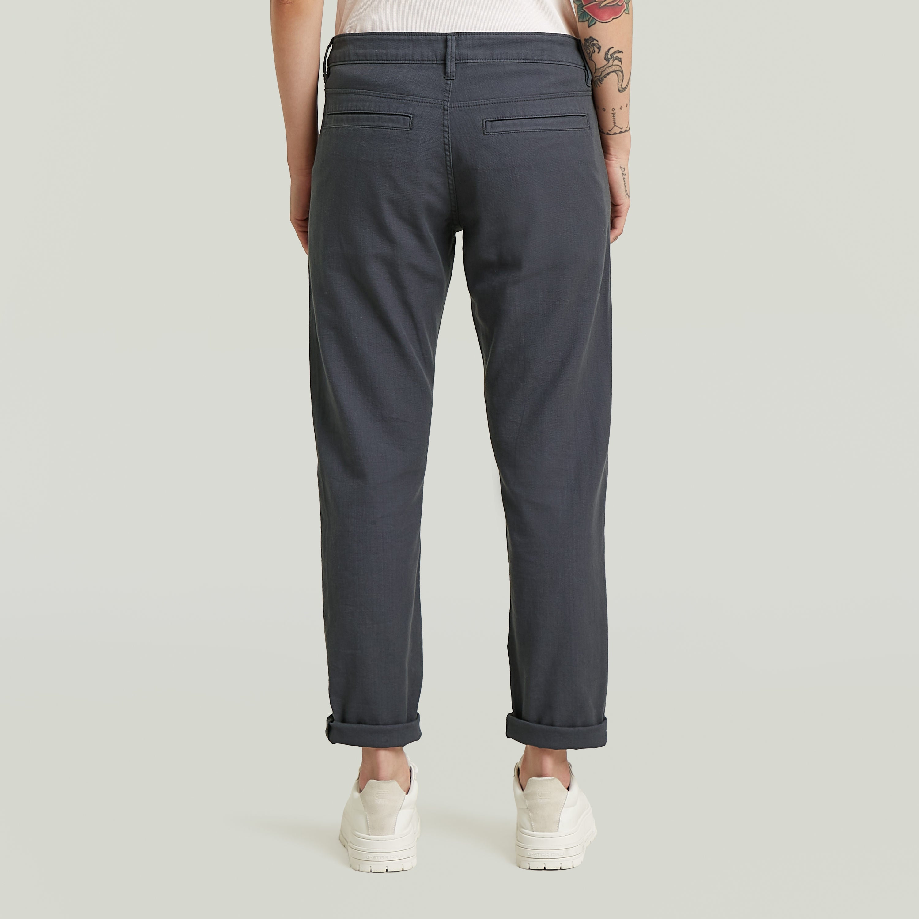 Mujer vista posterior usando los pantalones Kate boyfriend chinos, con perneras ligeramente estrechas y camisetas.