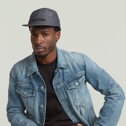 Hombre luciendo la gorra Flat Brim 5 Panel de G-STAR con chaqueta de mezclilla.