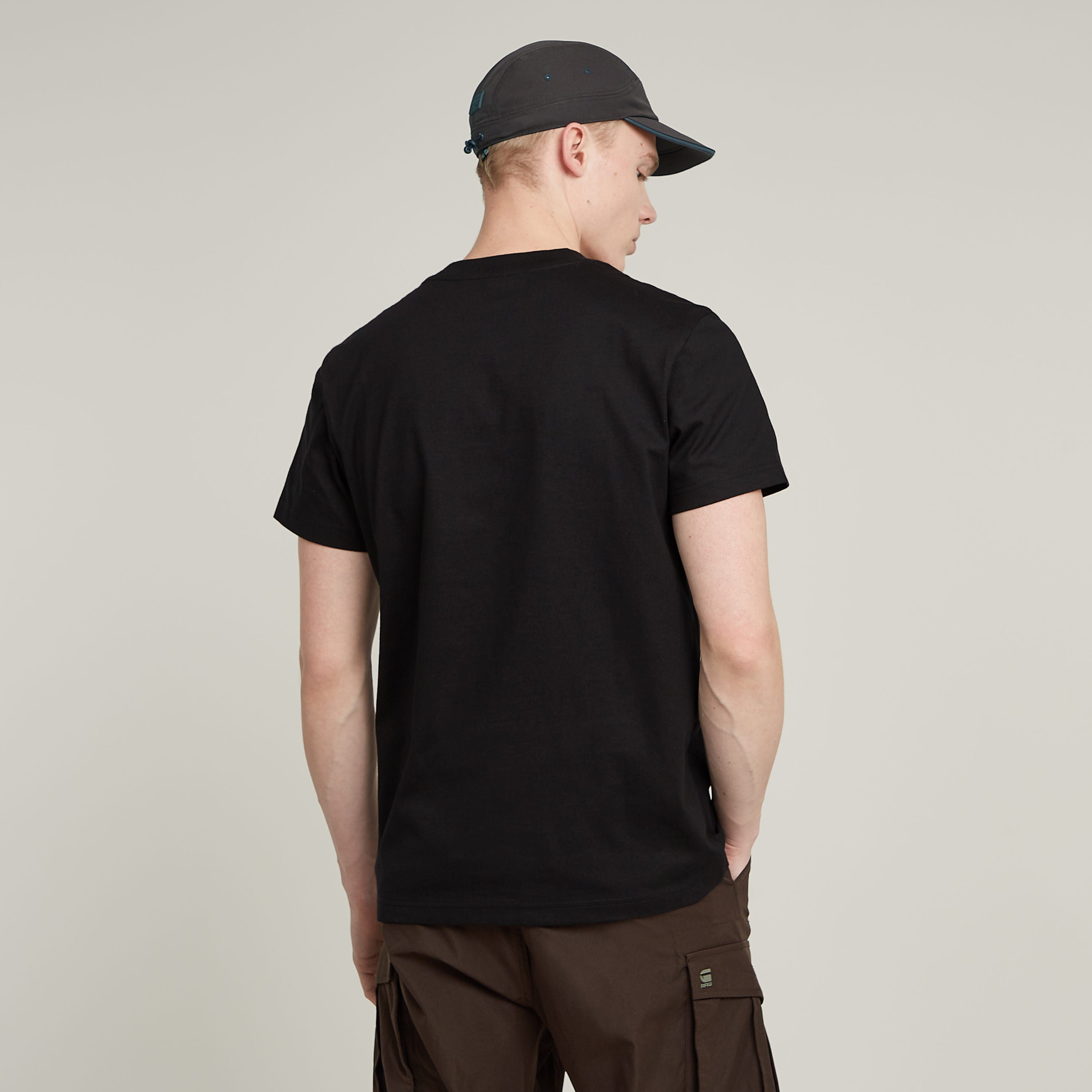 Hombre de espaldas vistiendo camiseta G-STAR con diseño gráfico negra y gorra.