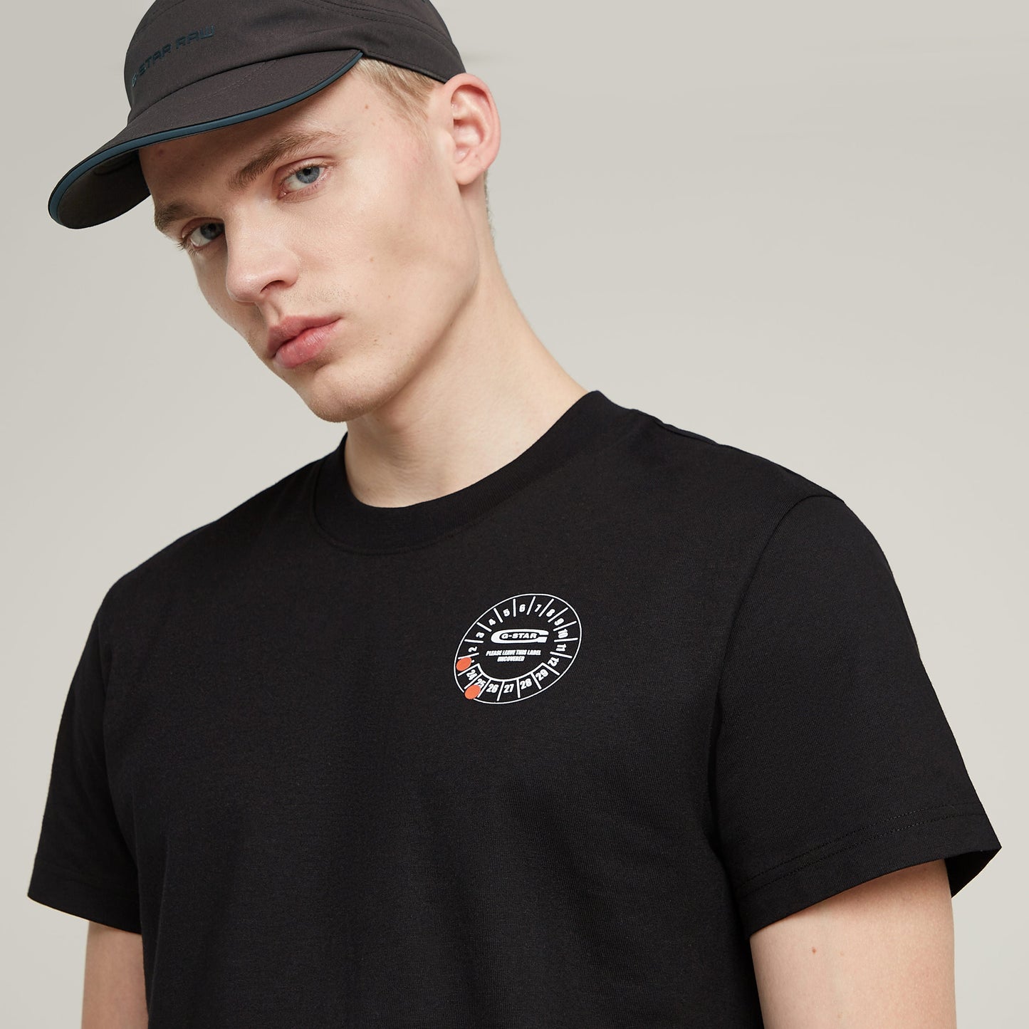 Modelo luciendo camiseta G-STAR con diseño gráfico y gorra, estampado distintivo en el pecho, estilo moderno.