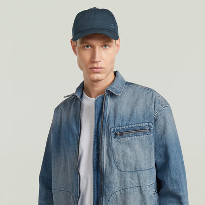 Gorra de béisbol Avernus en azul oscuro, modelo masculino con chaqueta de mezclilla y camiseta blanca.