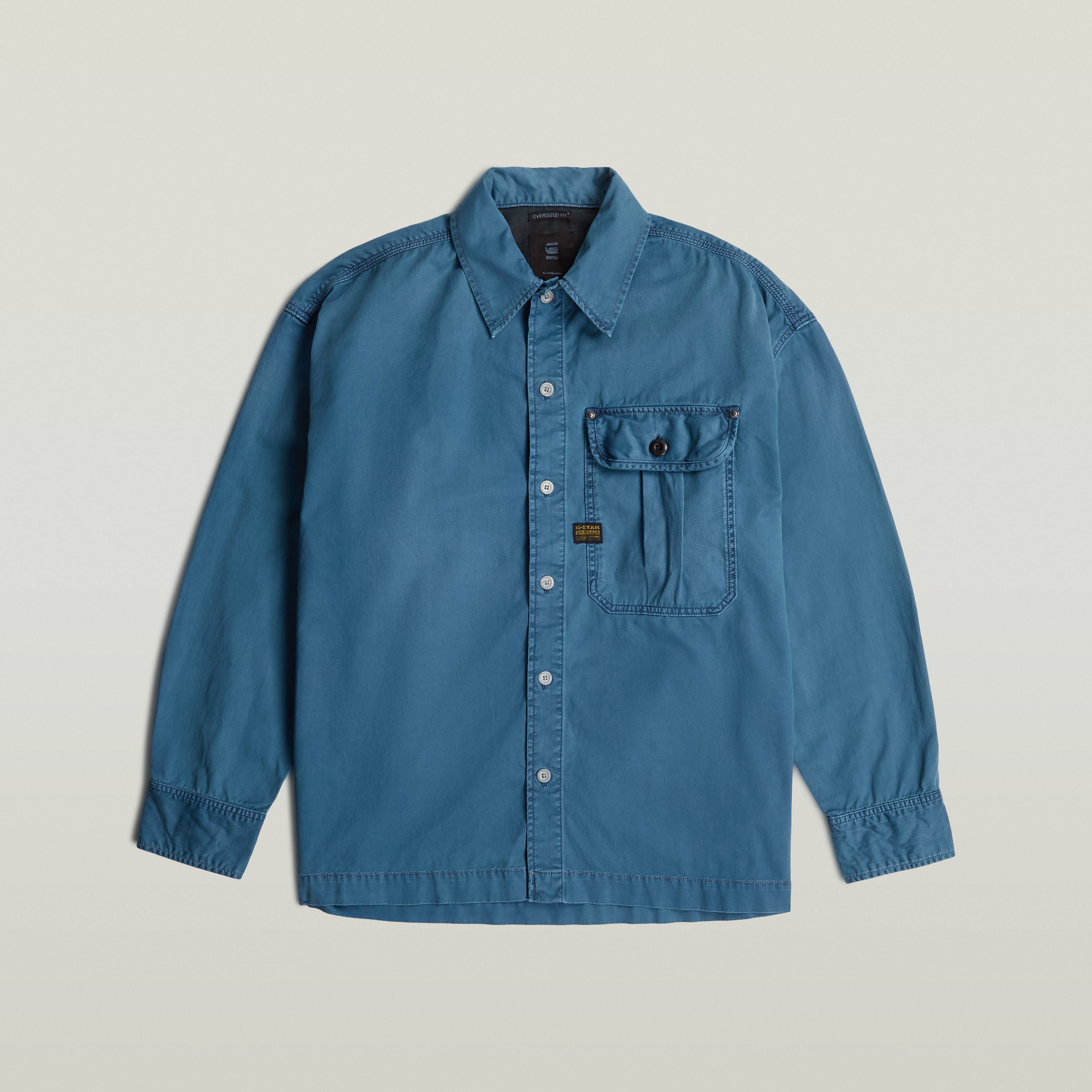Camisa plisada 1 Pocket Boxy, una boxy pleated shirt with pocket en color azul, corte relajado y detalles de diseño.