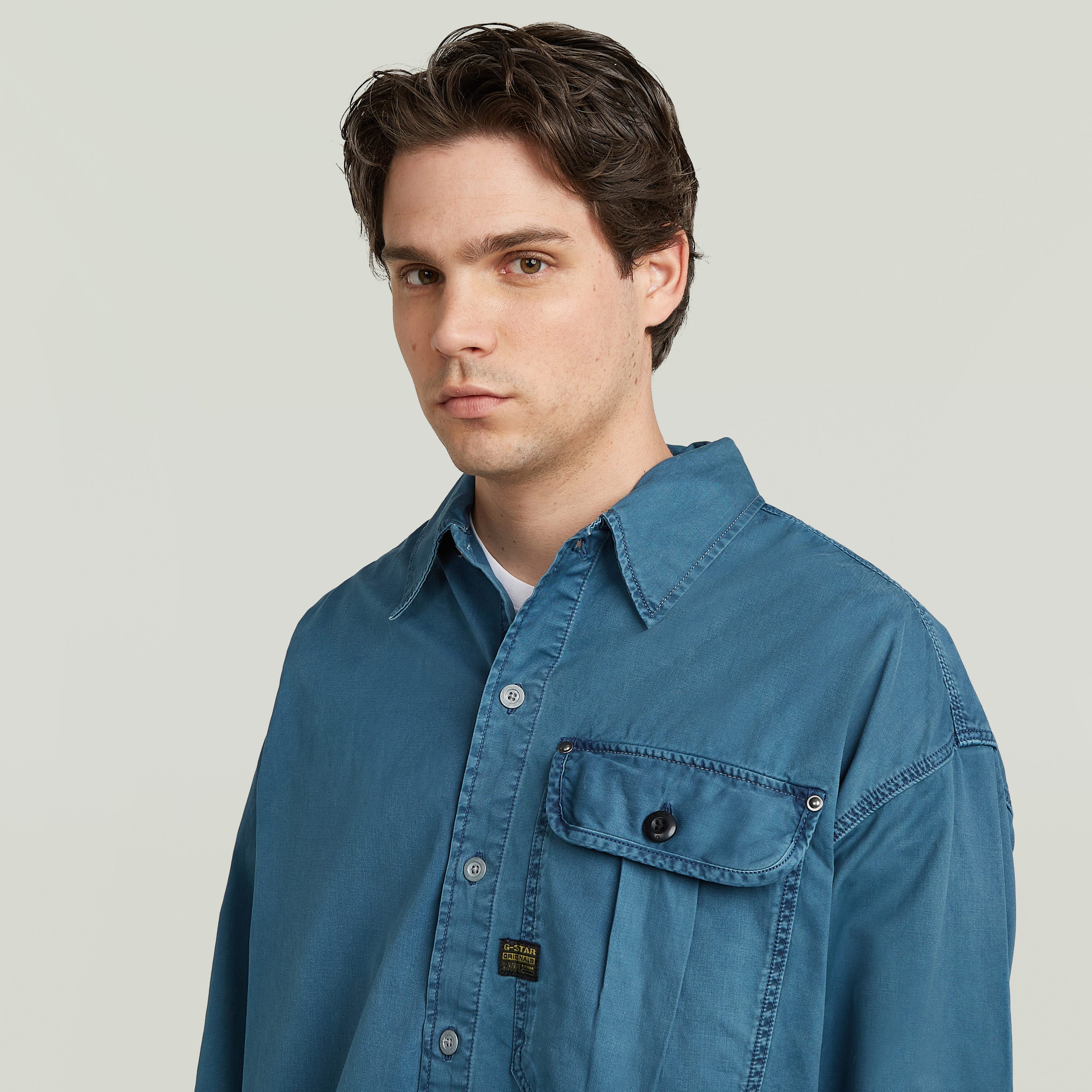 Modelo vistiendo una camisa boxy pleated shirt with pocket de color azul, con diseño relajado y un bolsillo en el pecho.