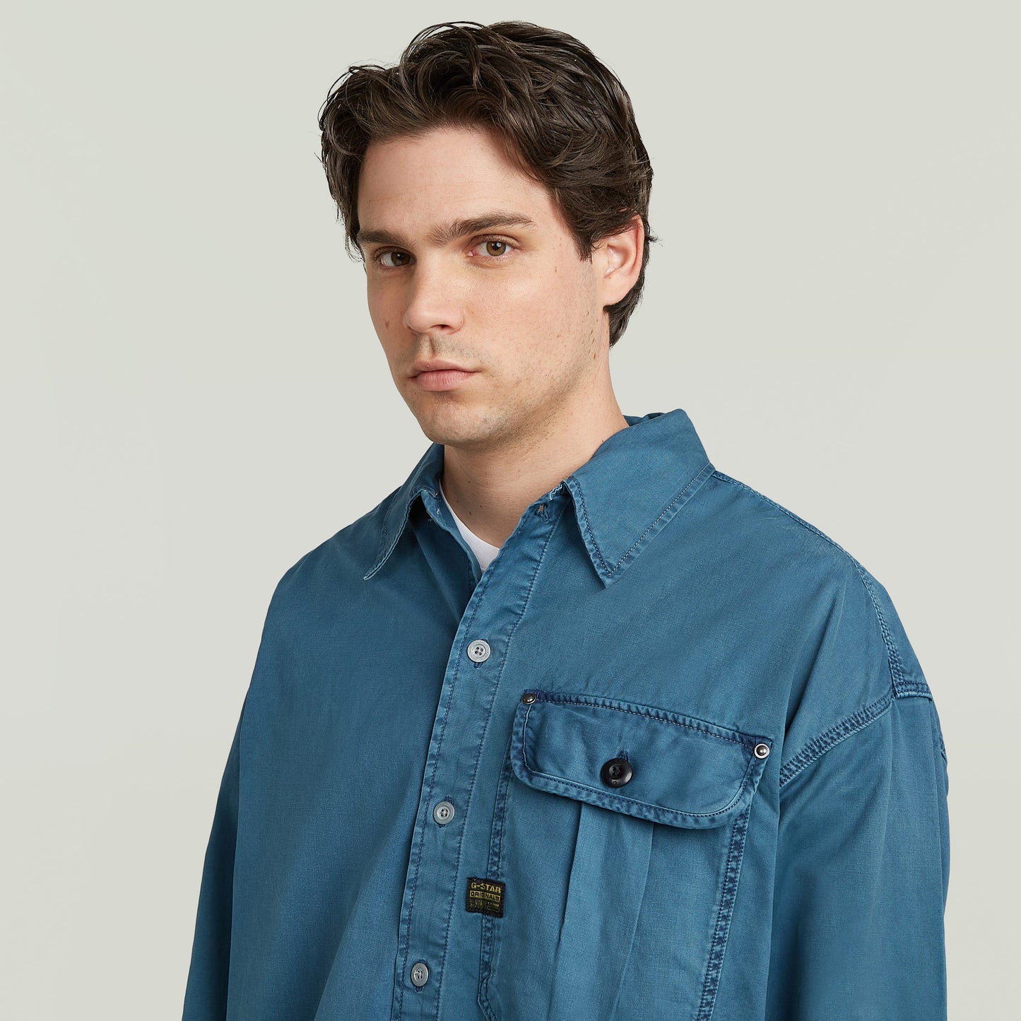Modelo vistiendo una camisa boxy pleated shirt with pocket de color azul, con diseño relajado y un bolsillo en el pecho.