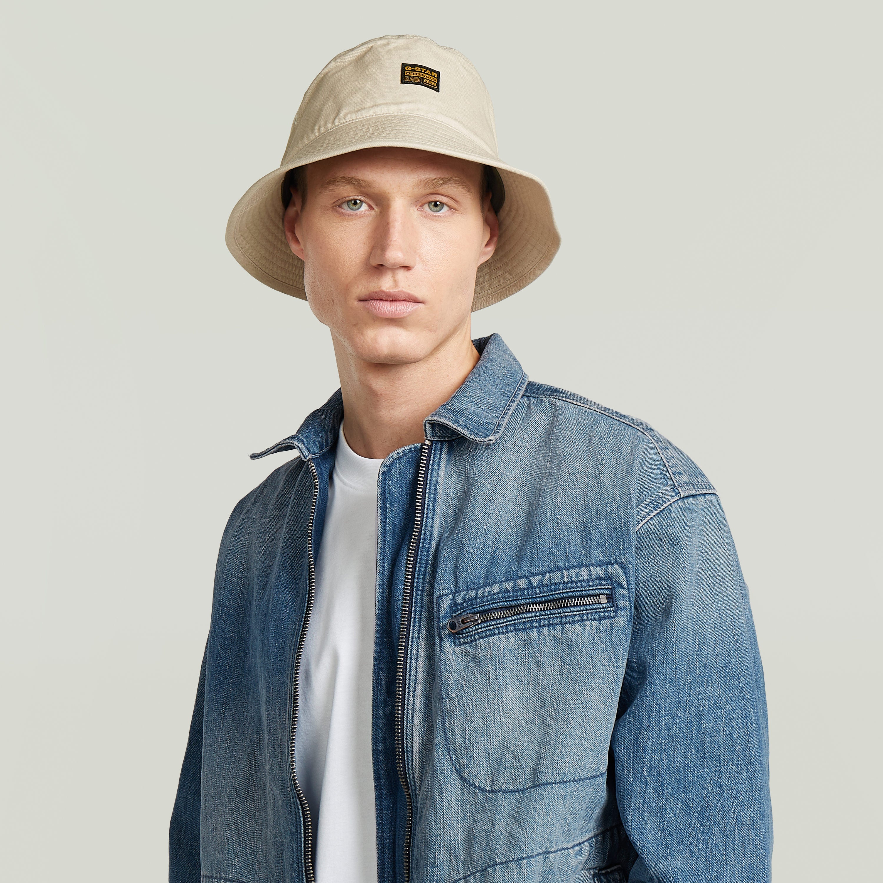 Modelo vistiendo sombrero de pescador G-STAR en color beige con chaqueta de denim.