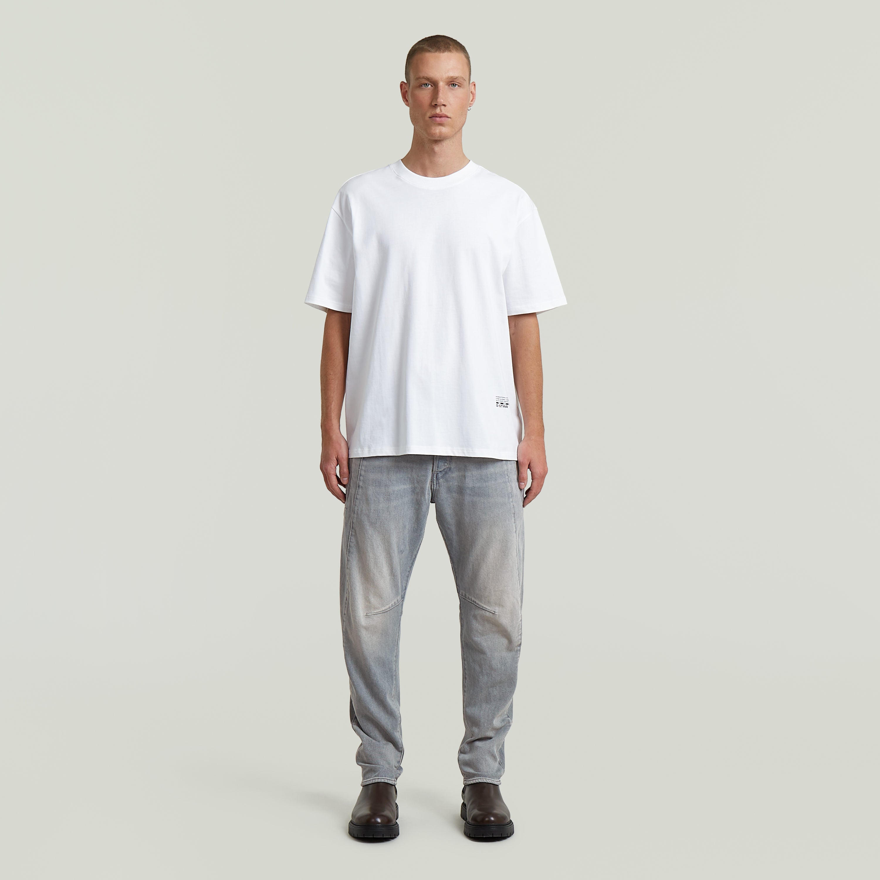 Hombre usando jeans Contor 3D Slim con camiseta blanca y botas negras frente a un fondo neutro.