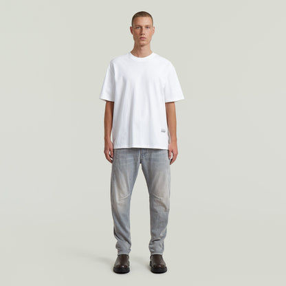 Hombre usando jeans Contor 3D Slim con camiseta blanca y botas negras frente a un fondo neutro.