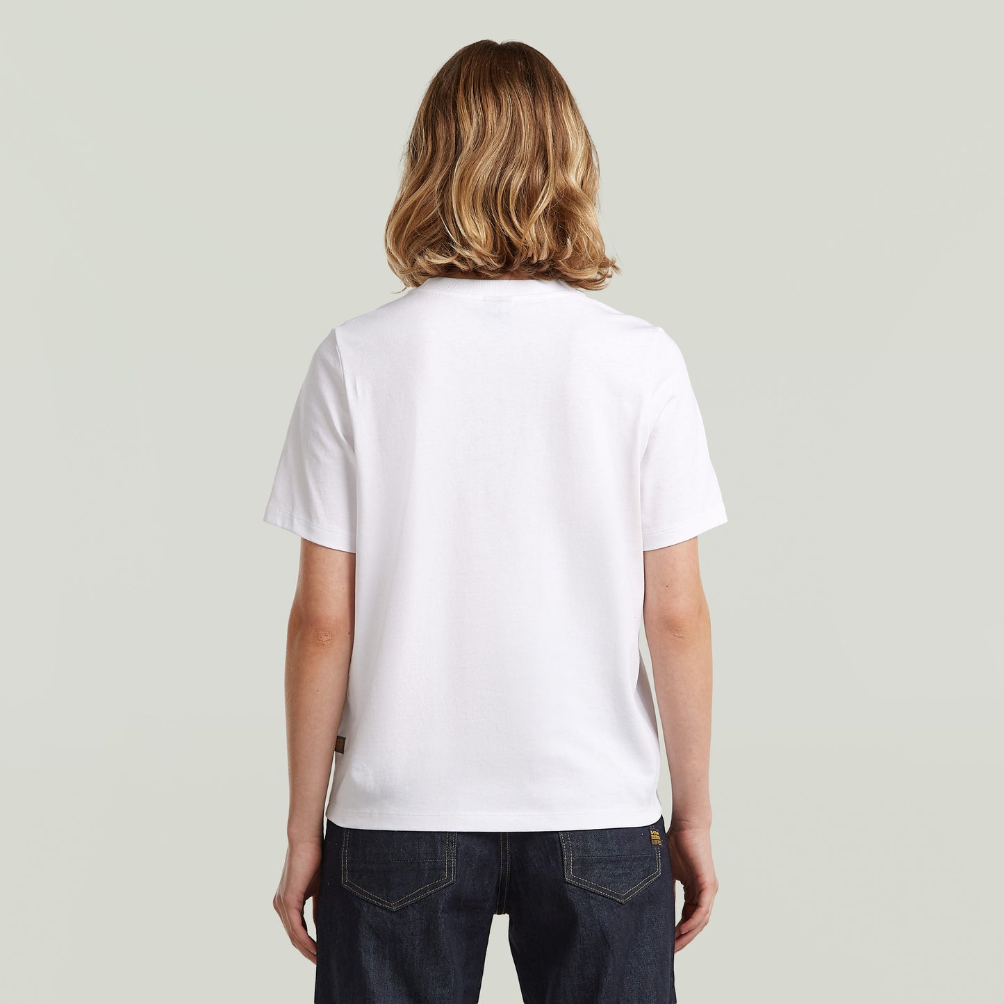 Parte posterior de una camiseta gráfica de algodón ecológico color blanco, con corte recto y manga corta.