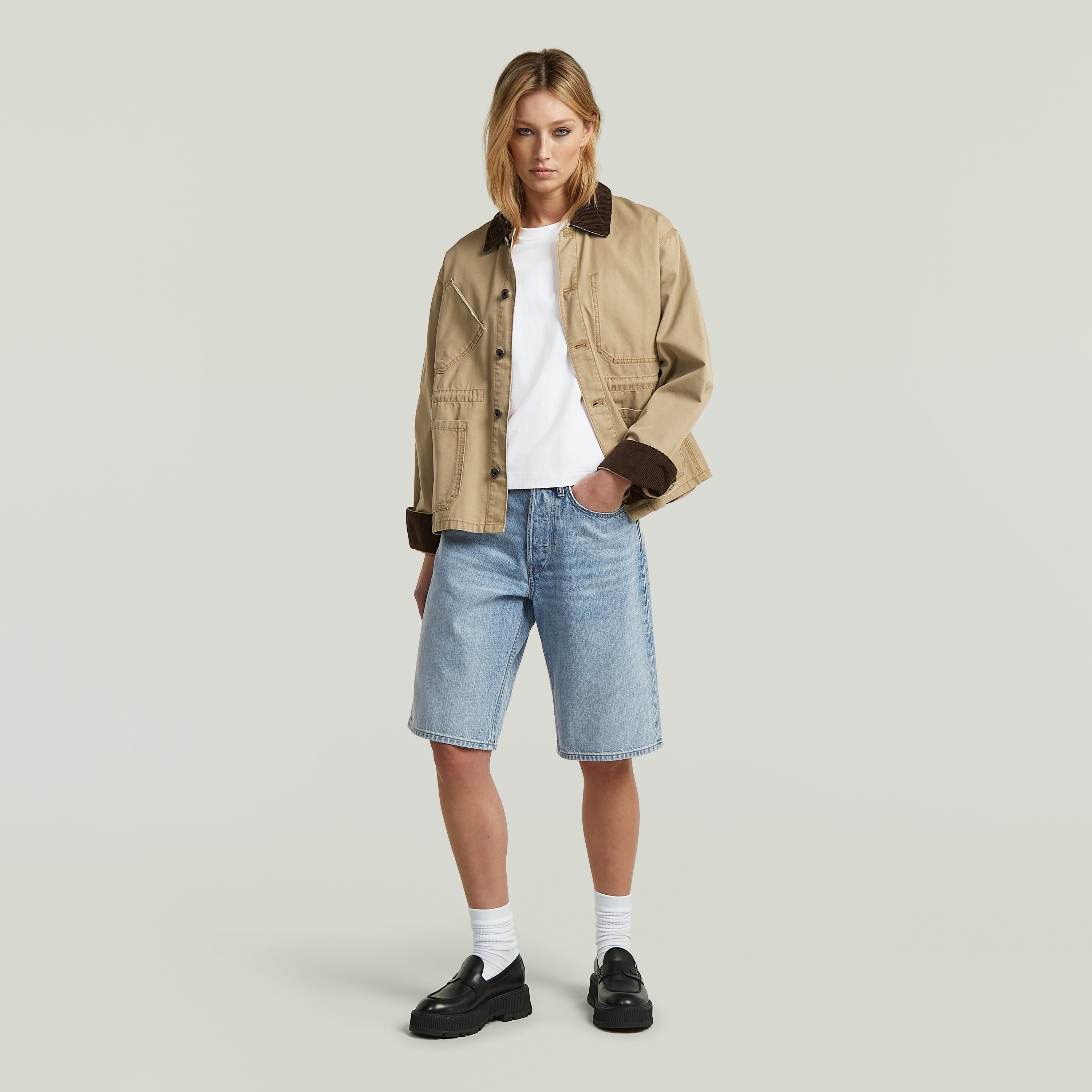 Mujer usando Bermuda Short Clean Edge con chaqueta beige y camiseta blanca, combinados con zapatos negros.