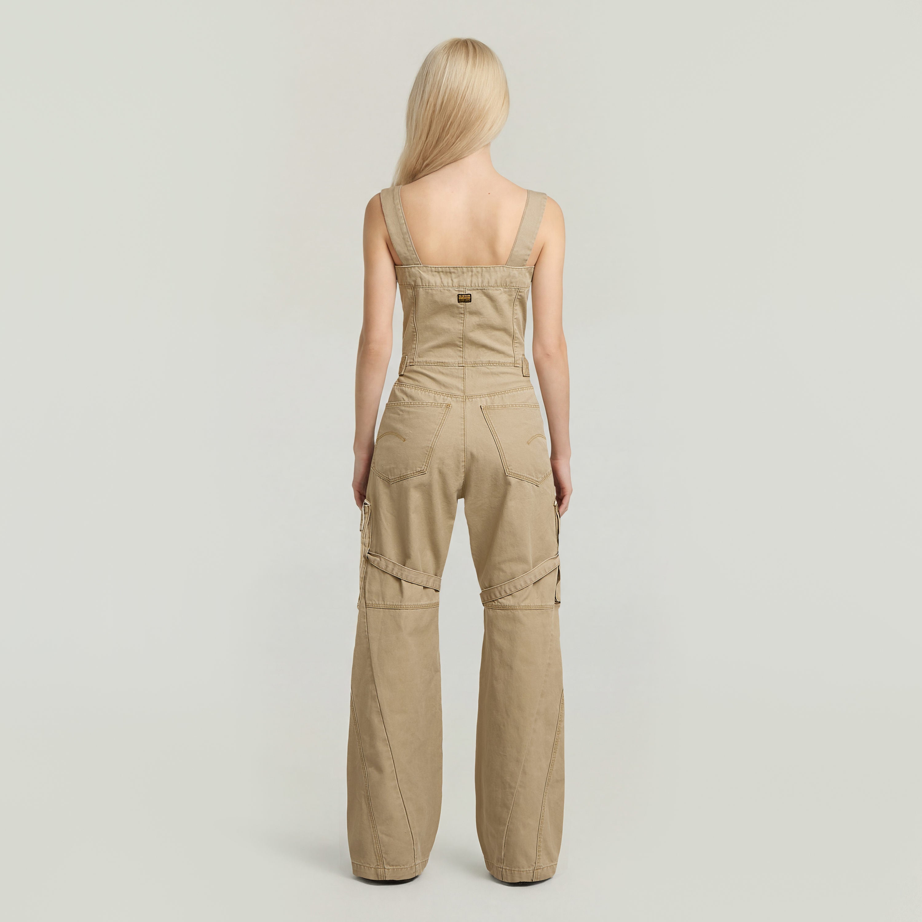 Mujer de espaldas vistiendo el elevated dungaree jumpsuit color beige con tiras racerback.