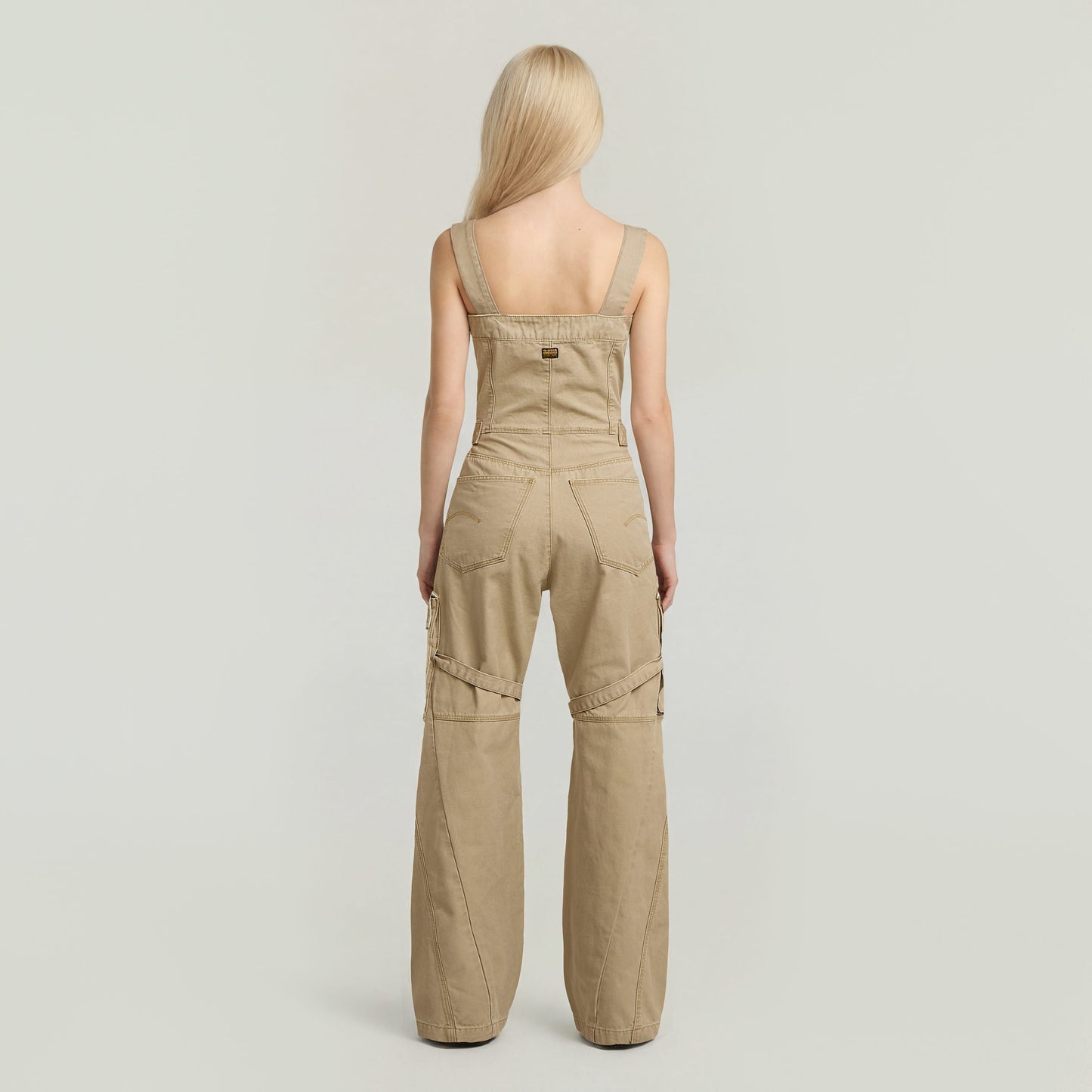 Mujer de espaldas vistiendo el elevated dungaree jumpsuit color beige con tiras racerback.