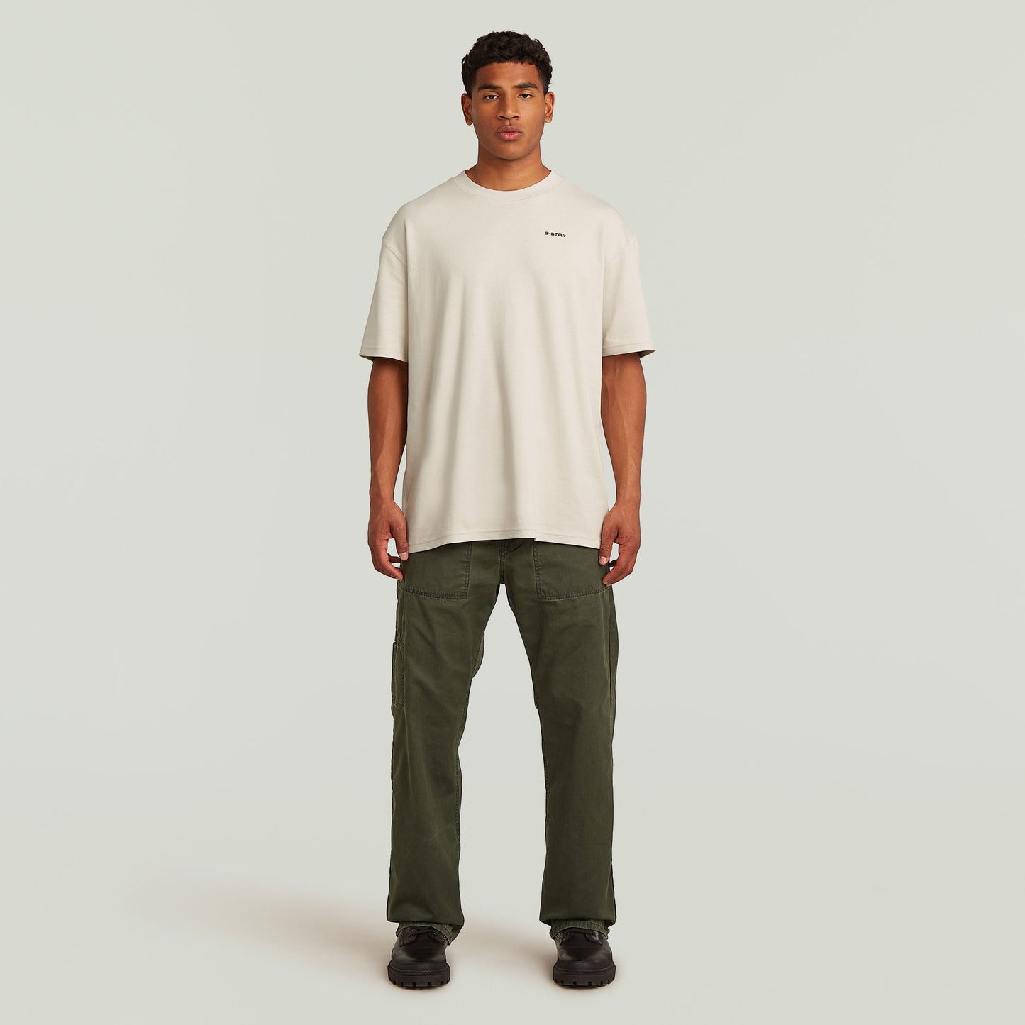 Modelo masculino vistiendo camiseta beige y pantalones chinos reversibles relaxed straight en color verde.